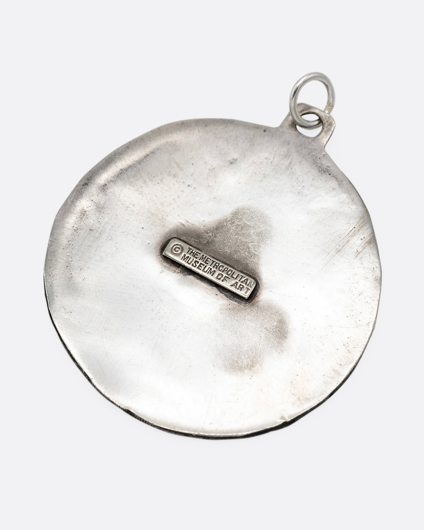 A silver medallion pendant with a smiling sun at the center. Shown from the back.