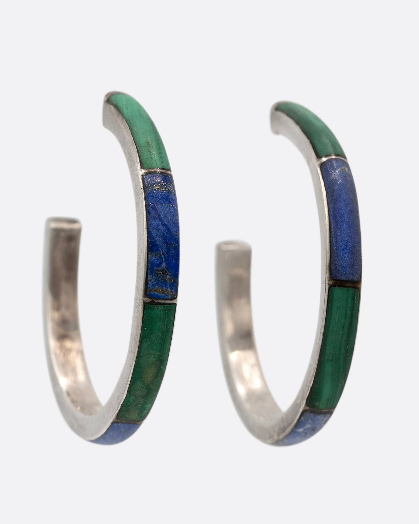 A pair of silver hoop earrings with malachite and lapis inlay. Shown at an angle from the front.