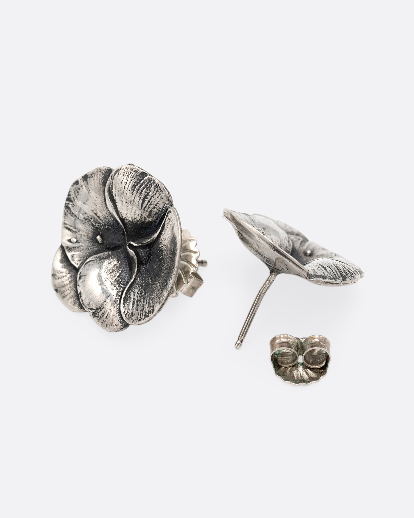 A pair of silver pansy earrings. One is shown from the front, the other from the back.
