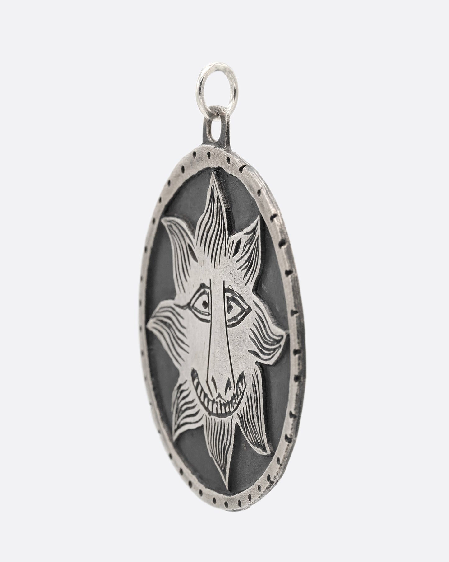 A silver medallion pendant with a smiling sun at the center. Shown from the side.