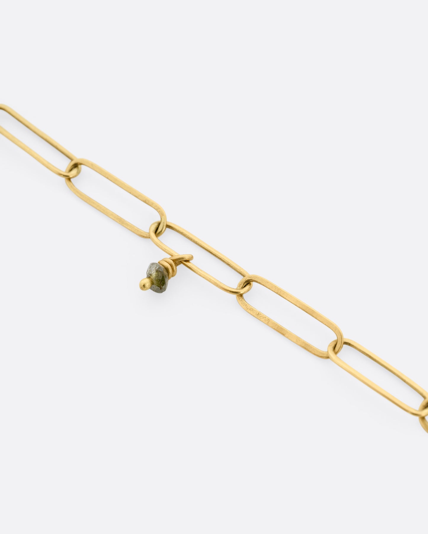 A close up of a yellow gold bracelet with popsicle stick-shaped links and green diamond beads scattered throughout.