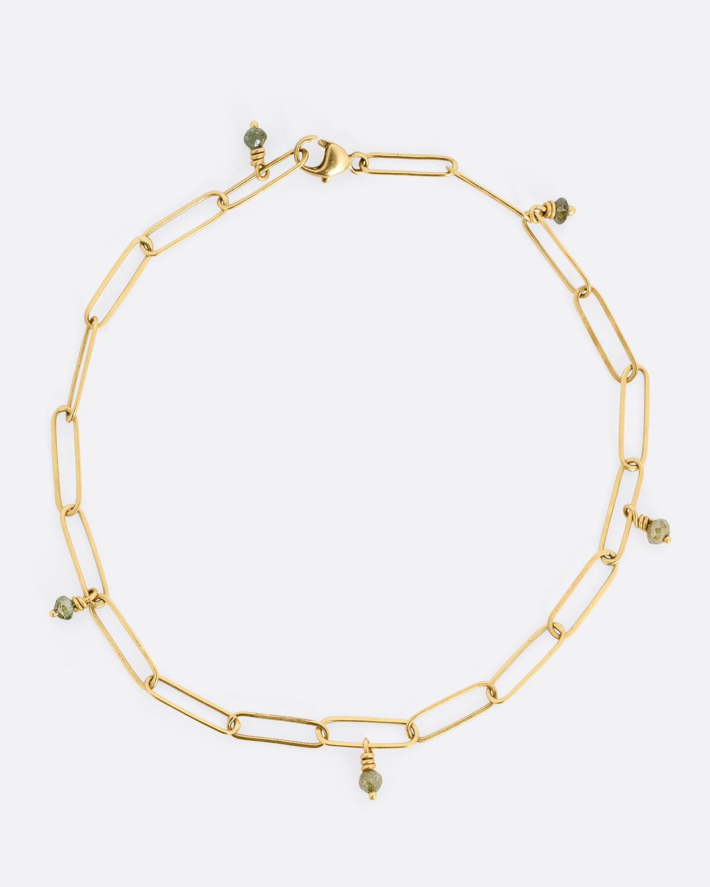 A bird's eye view of a yellow gold bracelet with popsicle stick-shaped links and green diamond beads scattered throughout.