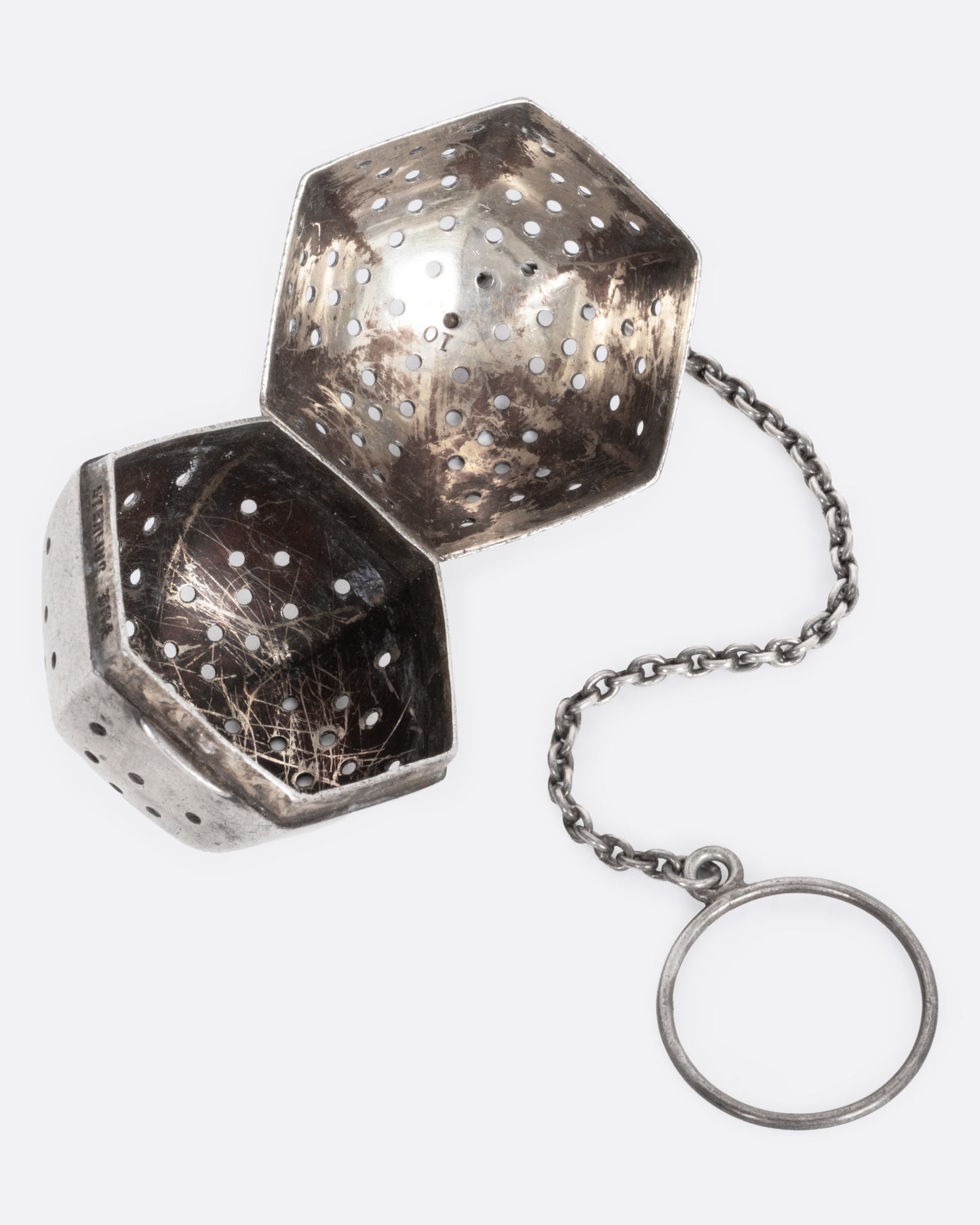 A hexagonal silver tea infuser with a chain, shown open from the side.