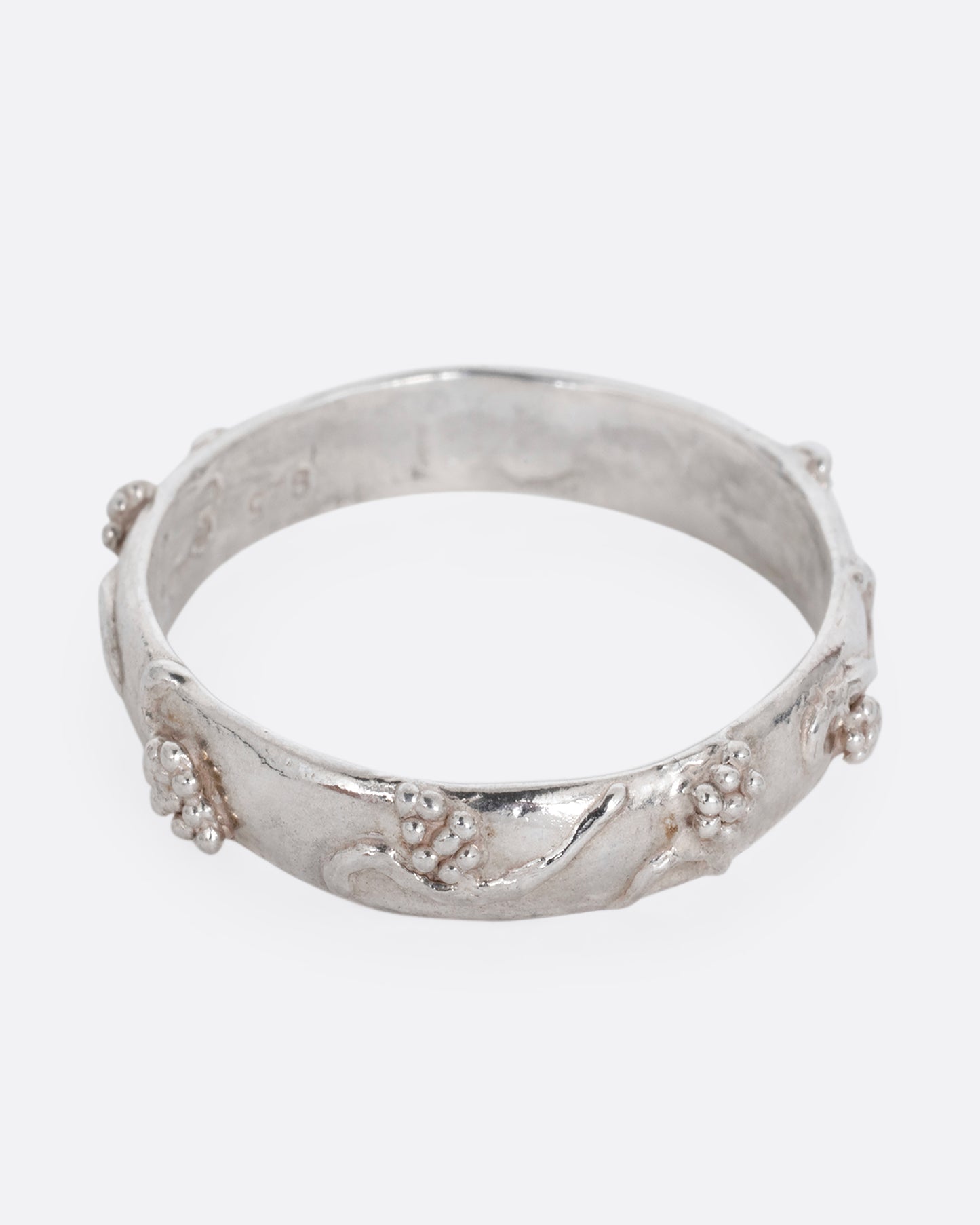 A silver ring with a grape vine motif. Shown from the front.
