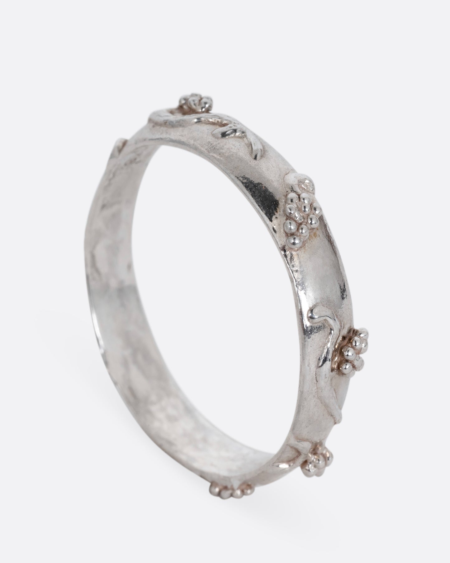 A silver ring with a grape vine motif. Shown from the side standing up.