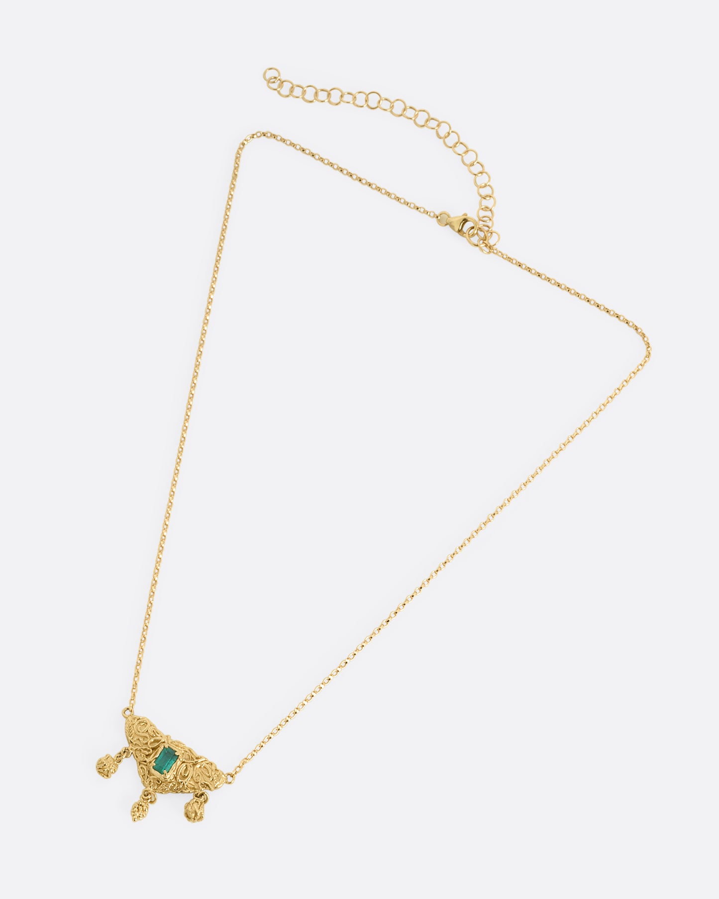 A yellow gold necklace with an emerald at the center of a sculptural pendant and three dangles- two blooming roses and a cluster of grapes. Shown from the front.
