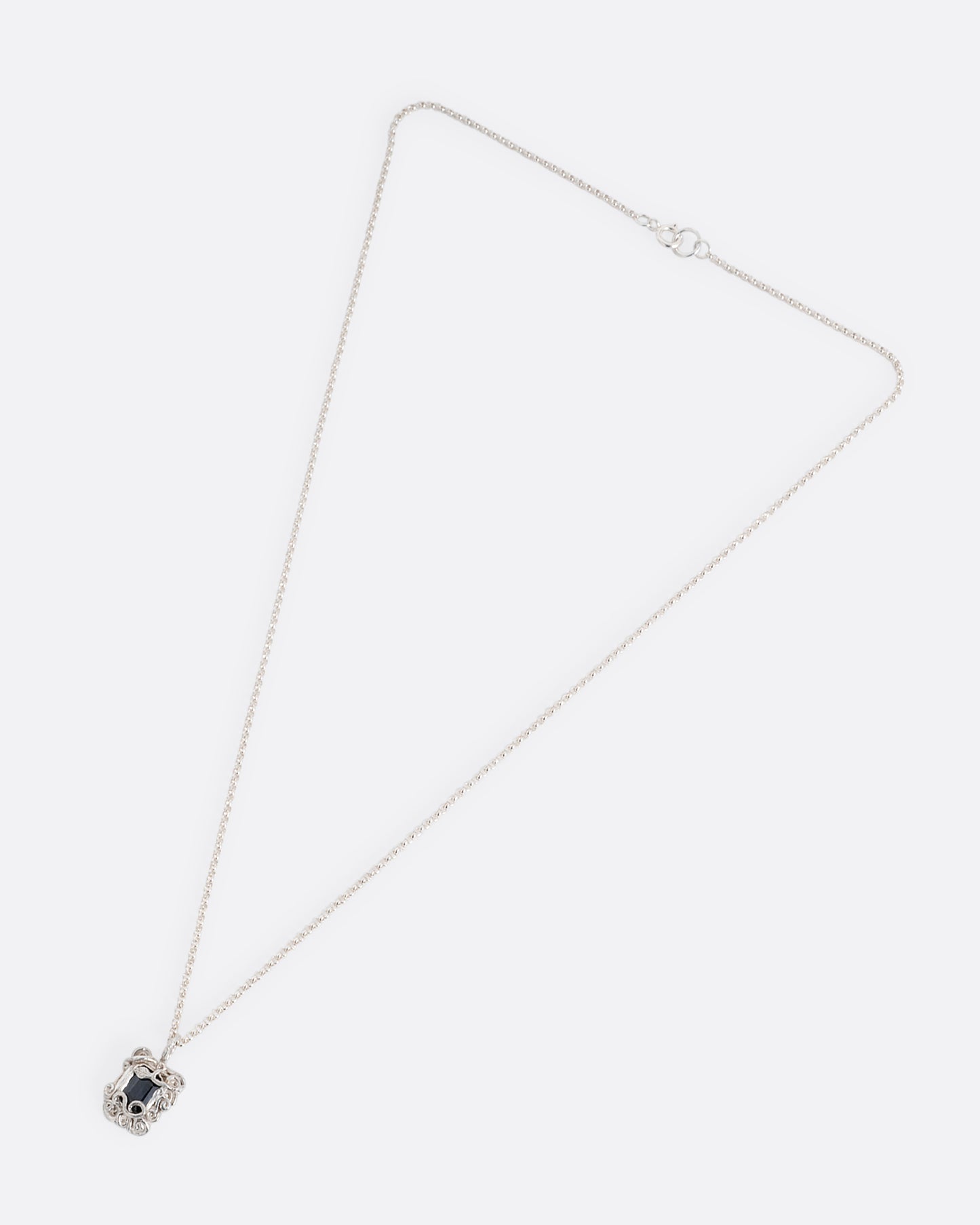 A silver pendant necklace with a deep blue sapphire in a setting with creeping vines. Shown from the front.