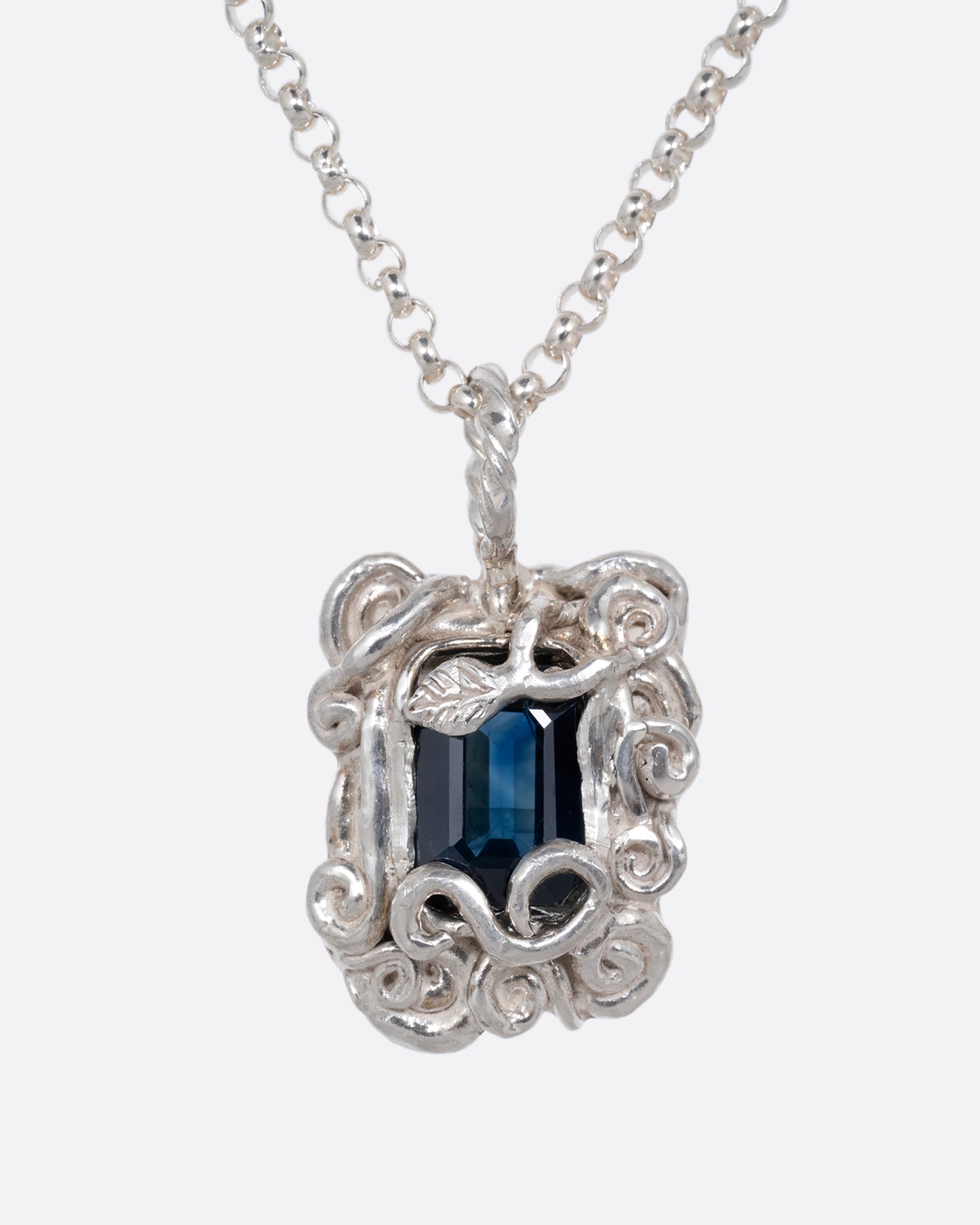 A silver pendant necklace with a deep blue sapphire in a setting with creeping vines. Shown from the front.
