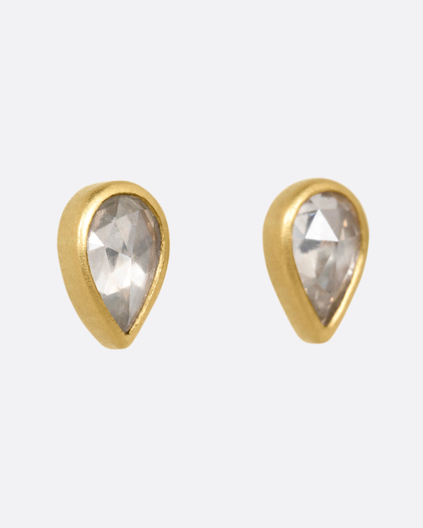A pair of yellow gold tear drop shaped stud earrings with diamonds. Shown from the side.