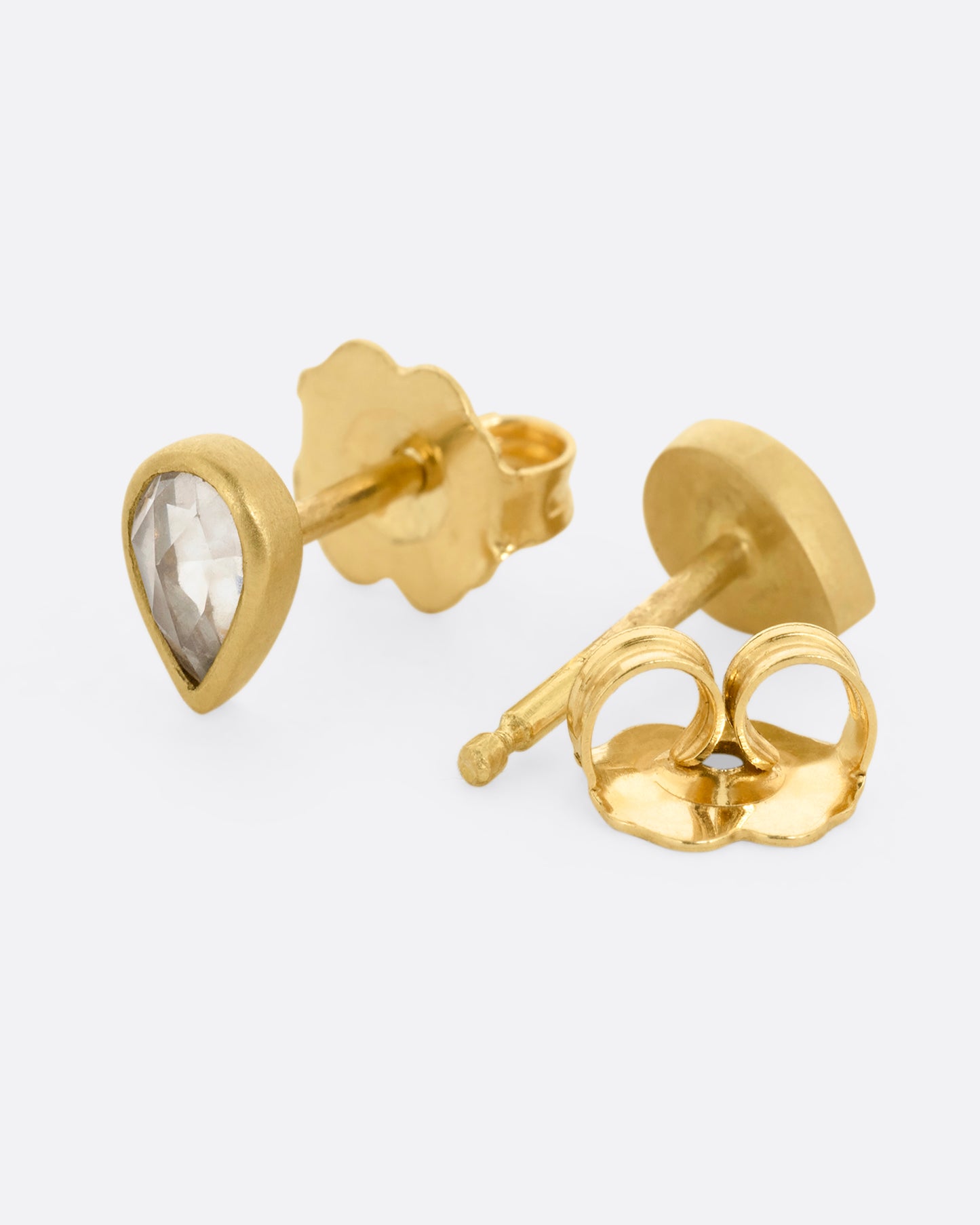 A pair of yellow gold tear drop shaped stud earrings with diamonds. Shown from the side. One earring is facing front, the other is facing back, open.