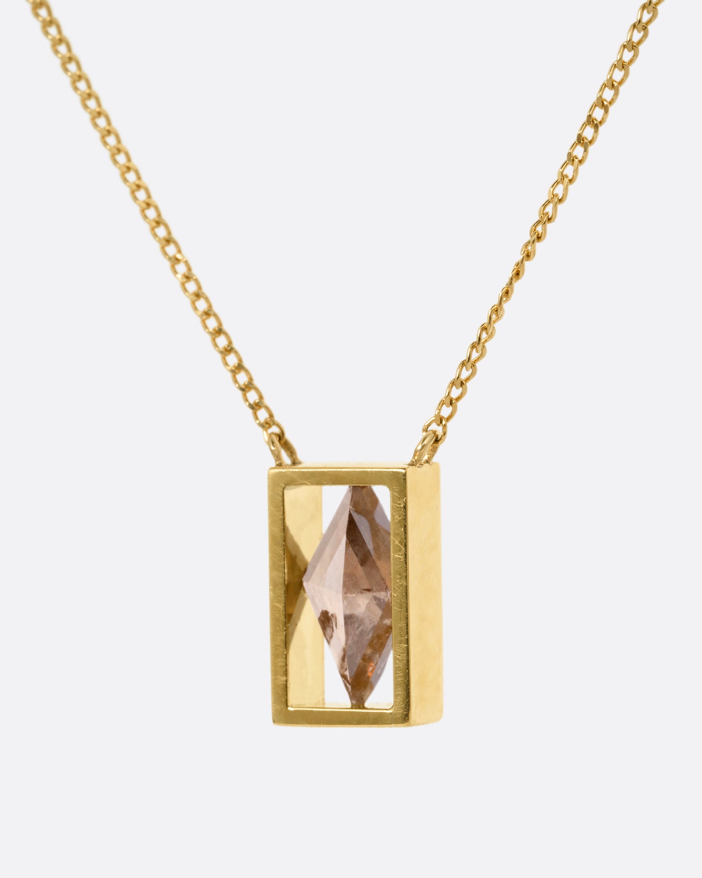 A yellow gold cable chain necklace with a rhombus shaped diamond in an open rectangular setting, shown from the side.