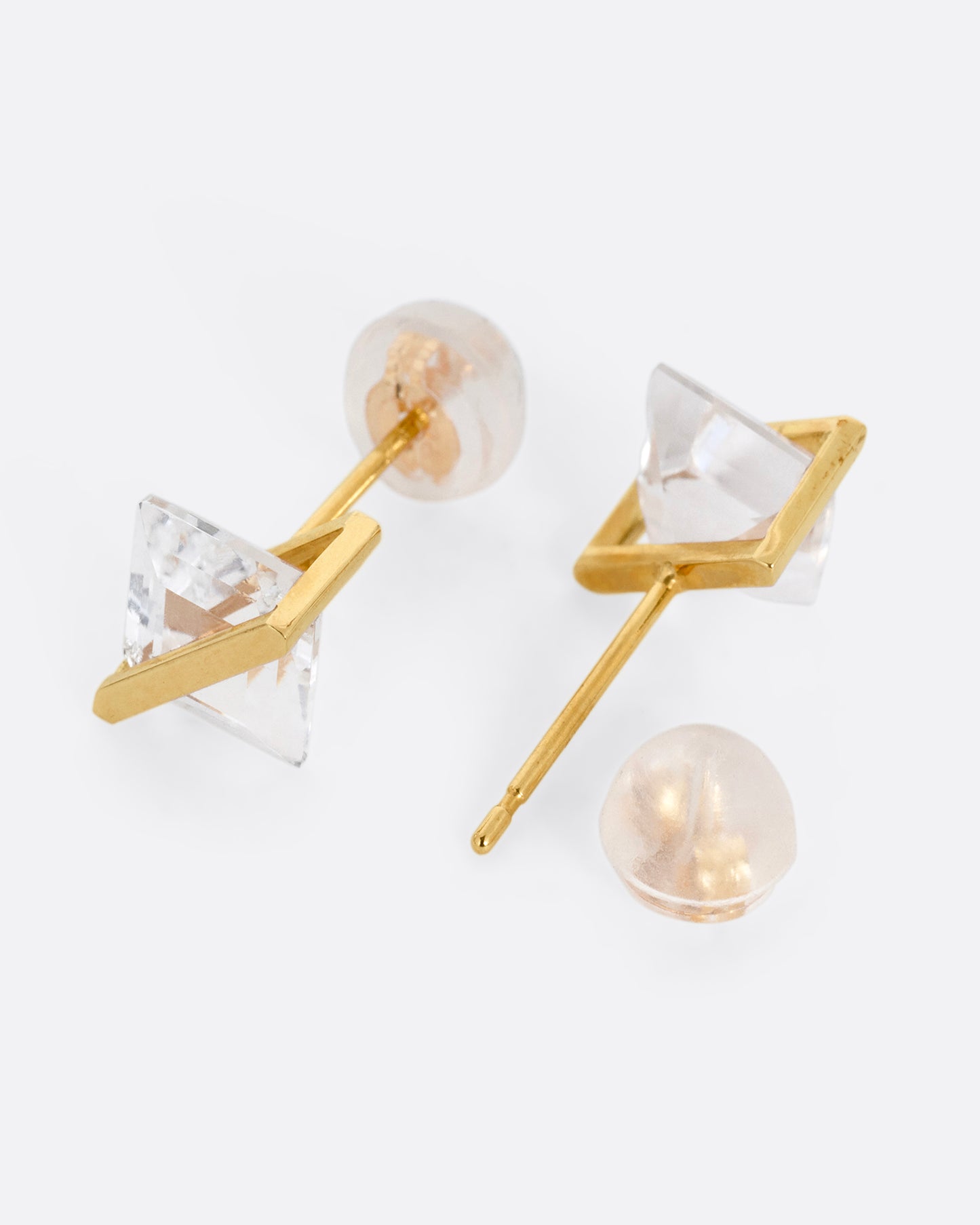 A pair of rhombus shaped quartzes, each in an open yellow gold bar stud earring setting. Shown lying on their sides with one earring open.