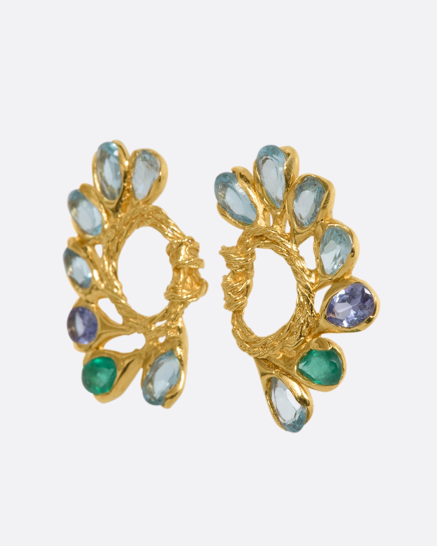 A pair of yellow gold circular twisted stud earrings feathered with oval emeralds, tanzanites, and topaz. View from the side.