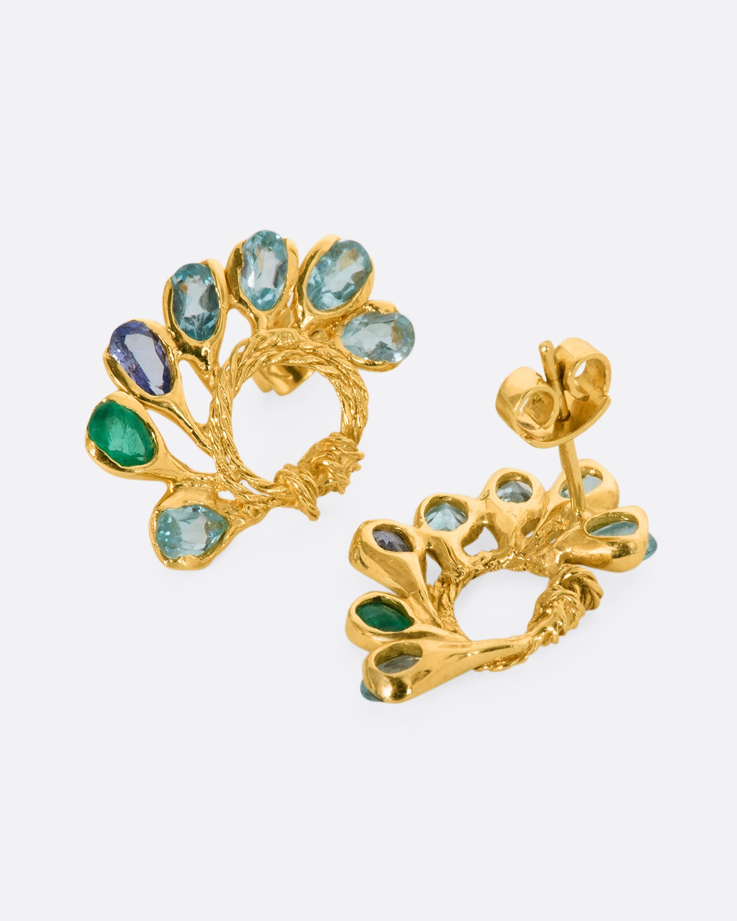A pair of yellow gold circular twisted stud earrings feathered with oval emeralds, tanzanites, and topaz. One is shown lying flat from the front, the other from the back.