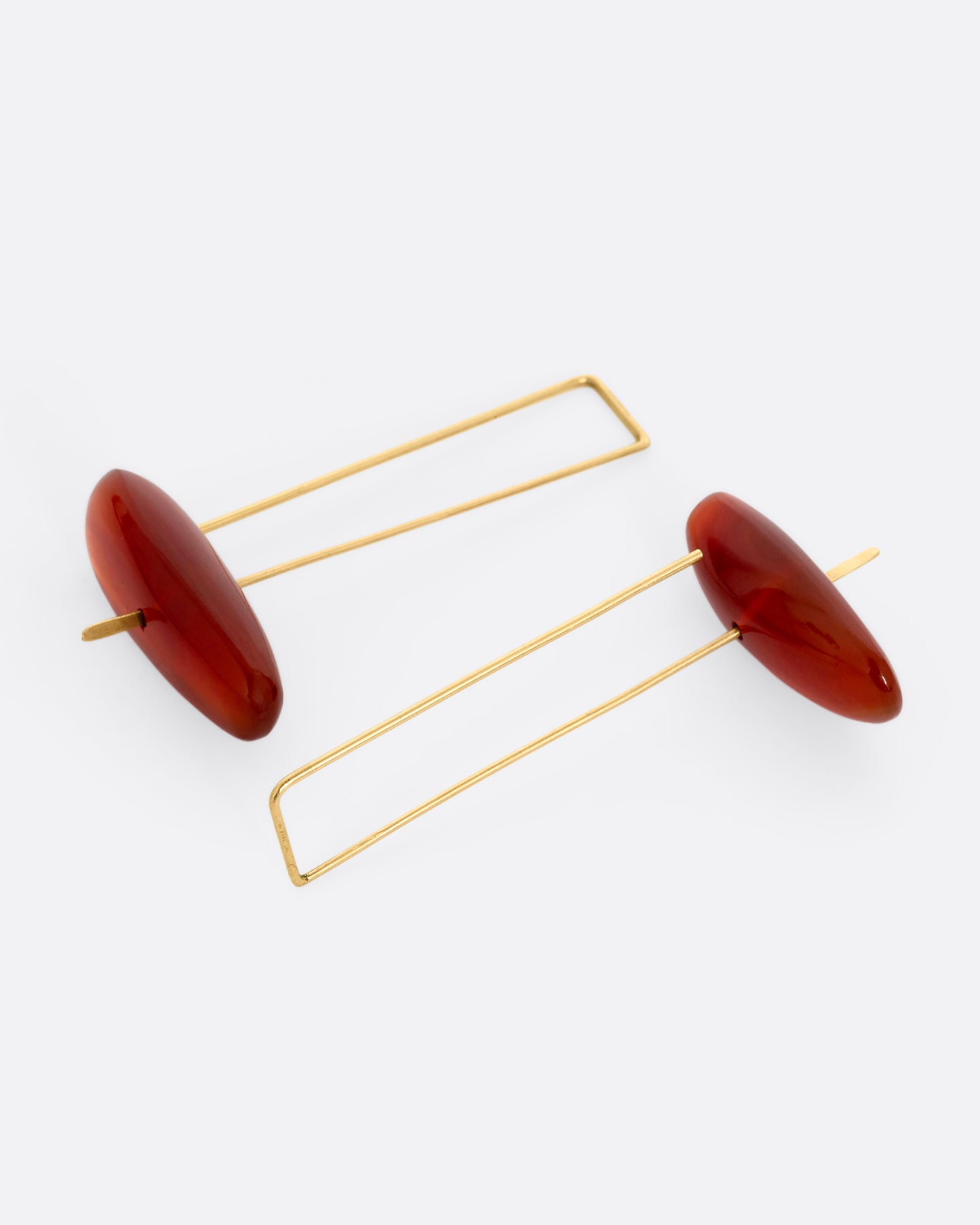 A pair of long yellow gold earrings with freeform carnelians at each base, shown lying flat.
