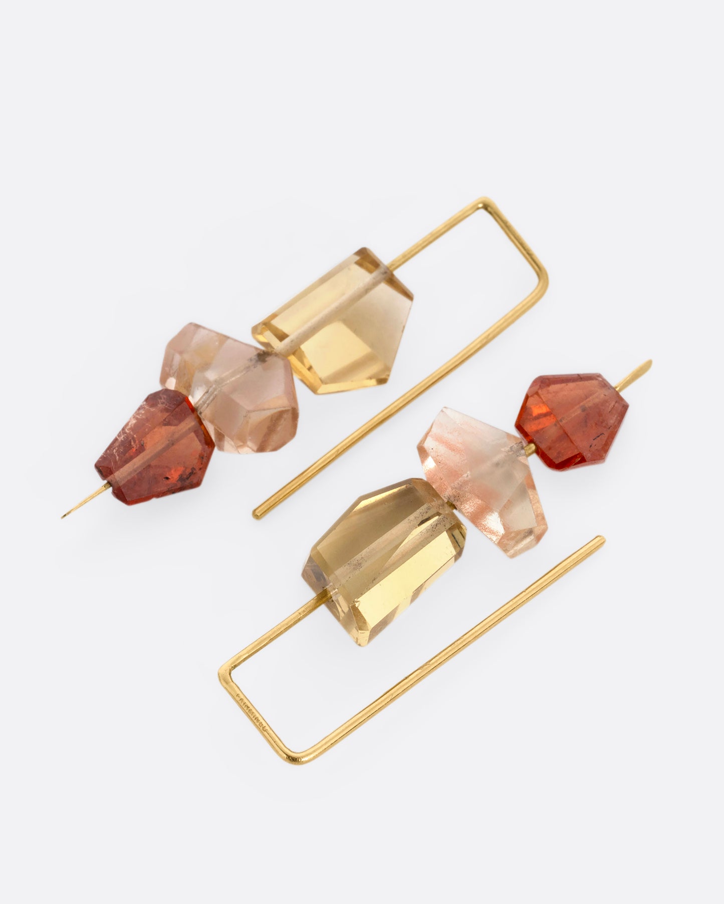 A pair of yellow gold hook earrings with a stack of three sunstones and hessonite garnets. Shown lying flat.
