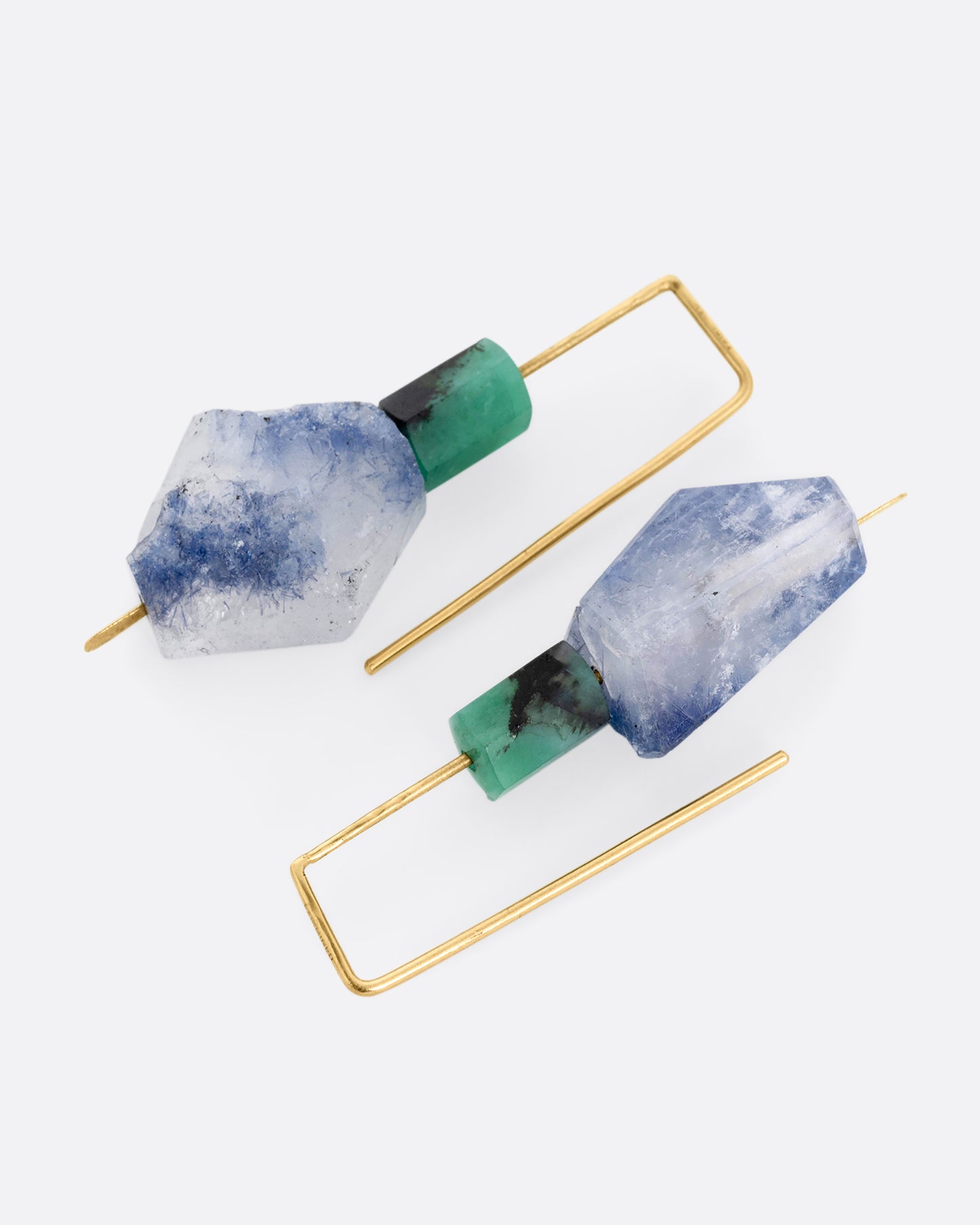 A pair of yellow gold hook earrings with a freeform dumortierite and emerald on each. Shown lying flat.