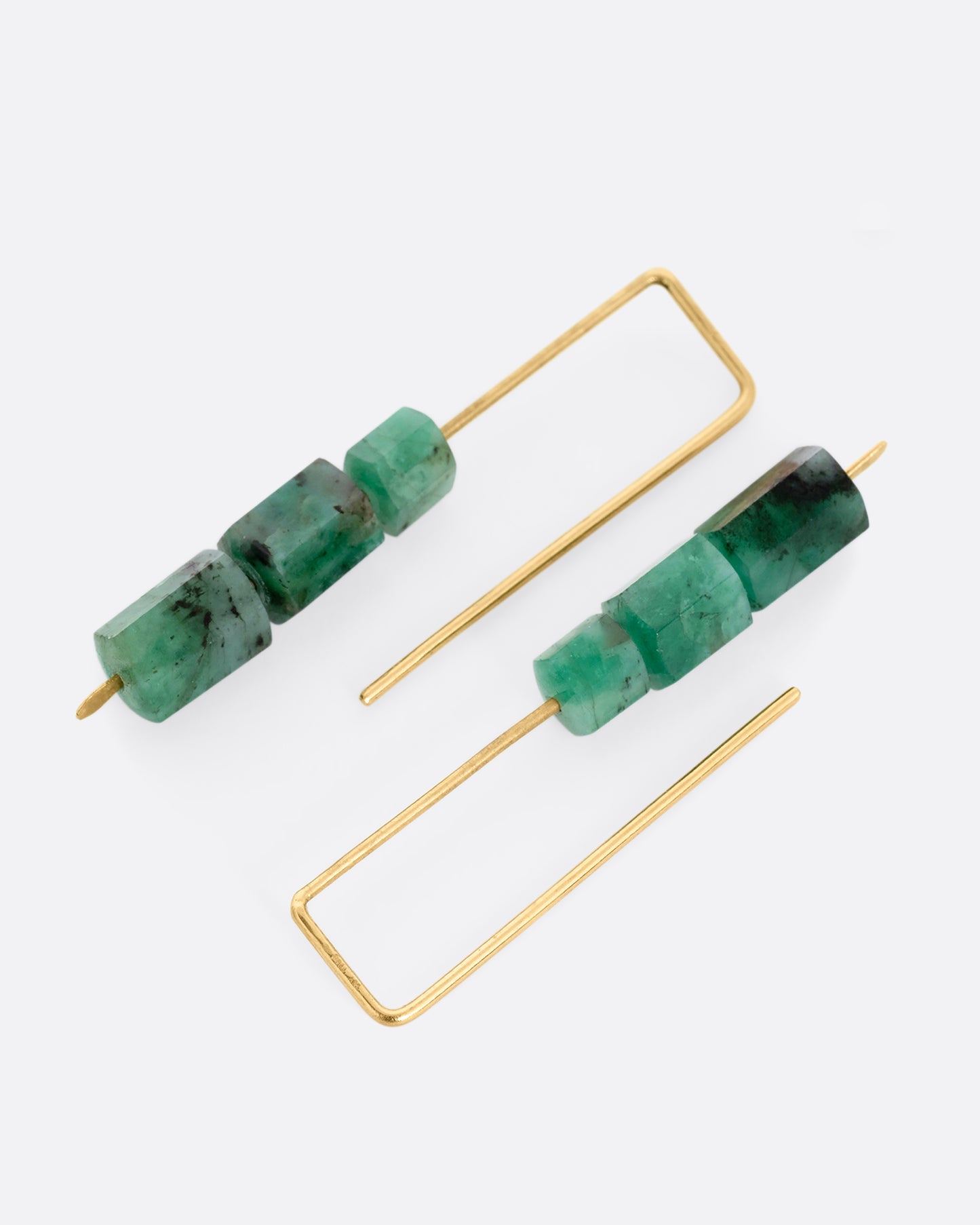 A pair of yellow gold hook earrings with three stacked freeform emeralds. Shown lying flat.