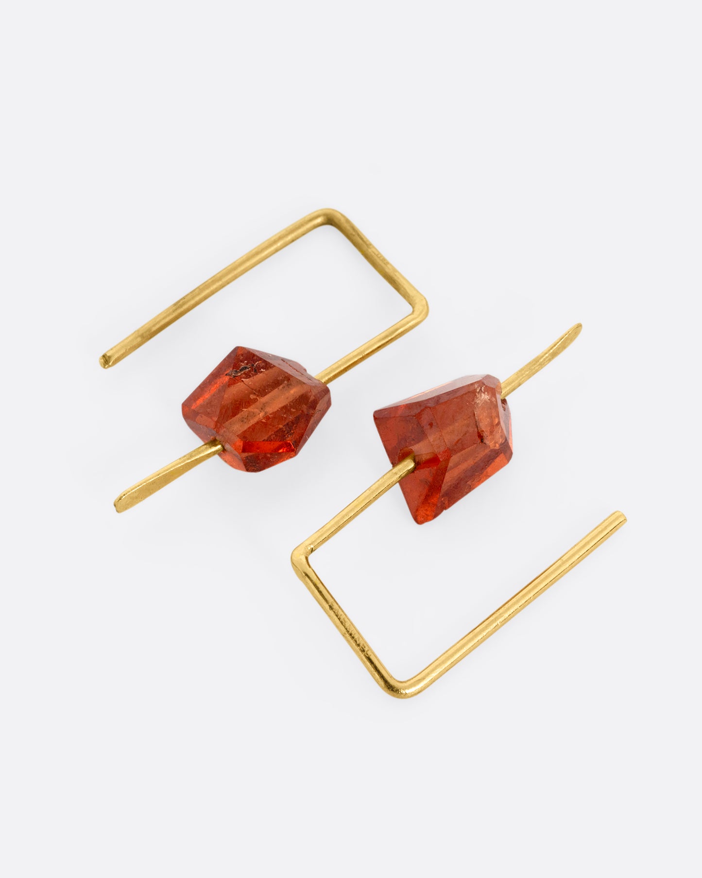 A pair of yellow gold hook earrings with angular hessonite garnets, shown lying flat.