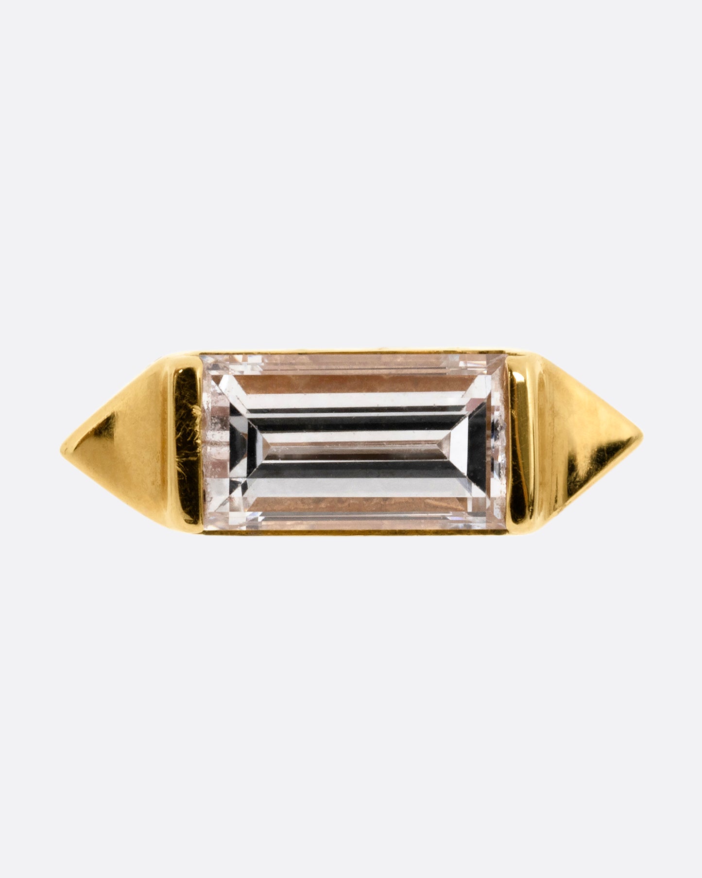 A yellow gold stud earring with a baguette diamond, bookended with points. Shown from the front.