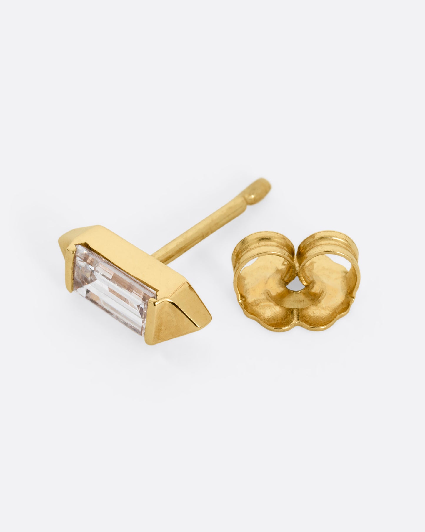 A yellow gold stud earring with a baguette diamond, bookended with points. Shown open on its side.