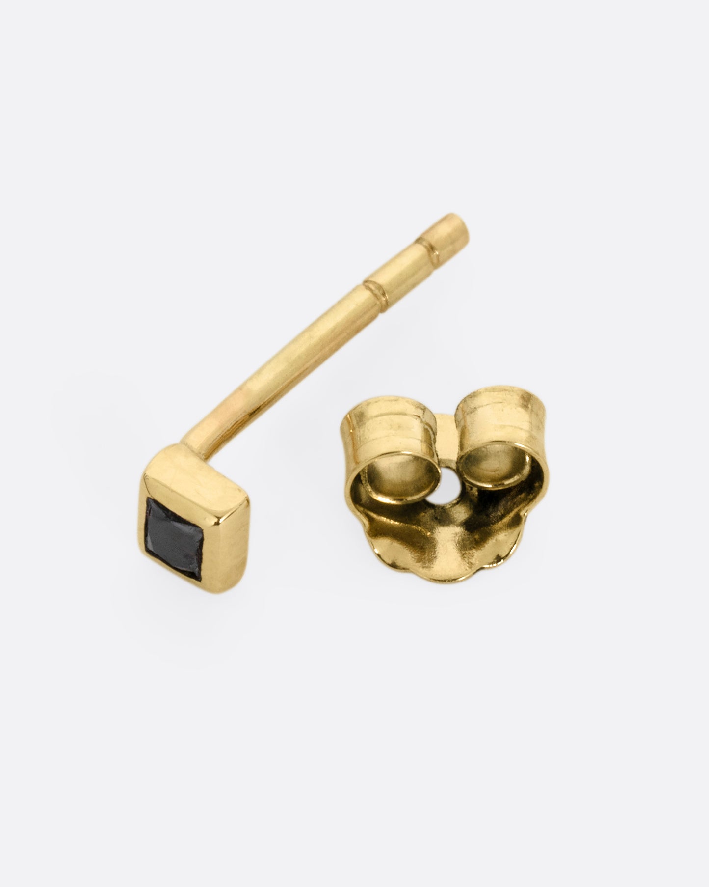 A yellow gold stud earring with a princess cut black diamond, shown open on it side.