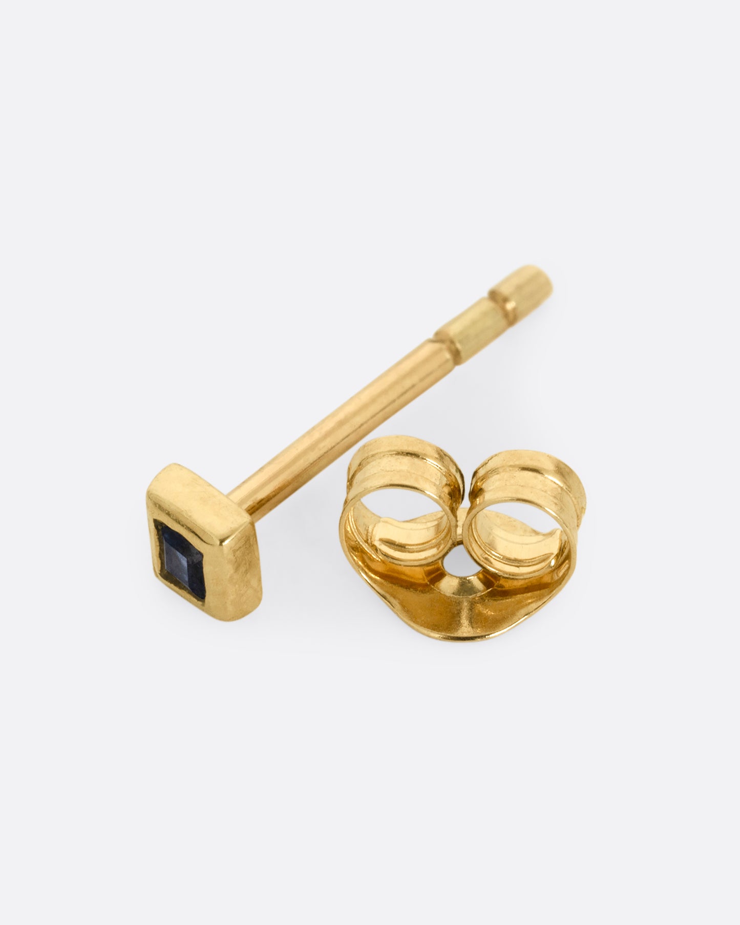 A yellow gold stud earring with a princess cut sapphire. Shown open on its side.