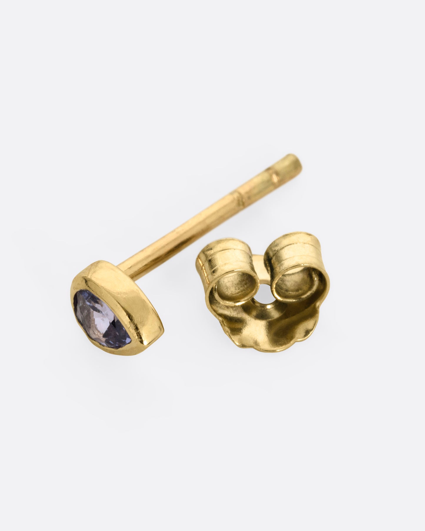 A yellow gold teardrop shaped bezel set tanzanite stud earring. Shown open on its side.