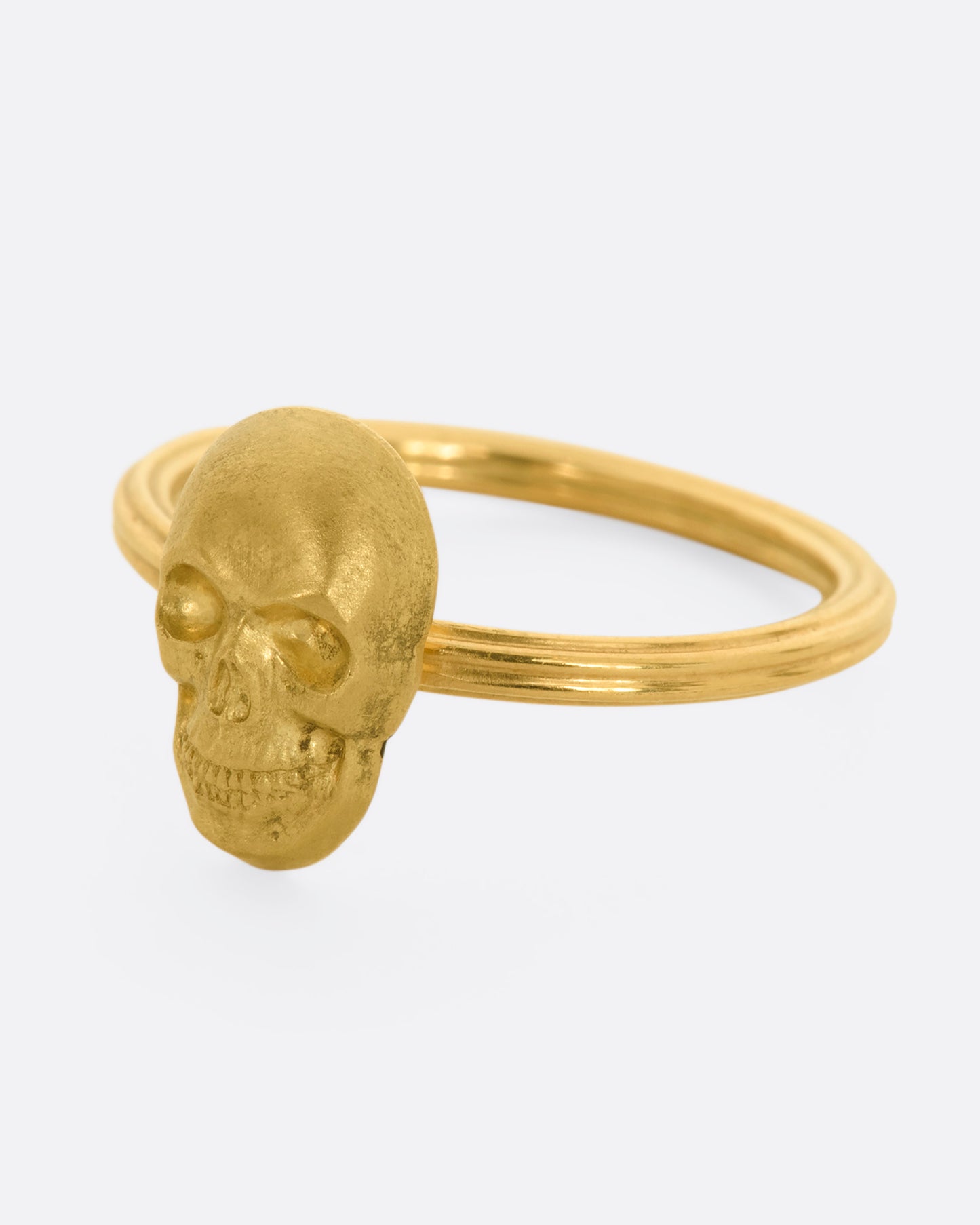 Side view of yellow gold ring with a sculpted skull charm on a round fluted band.