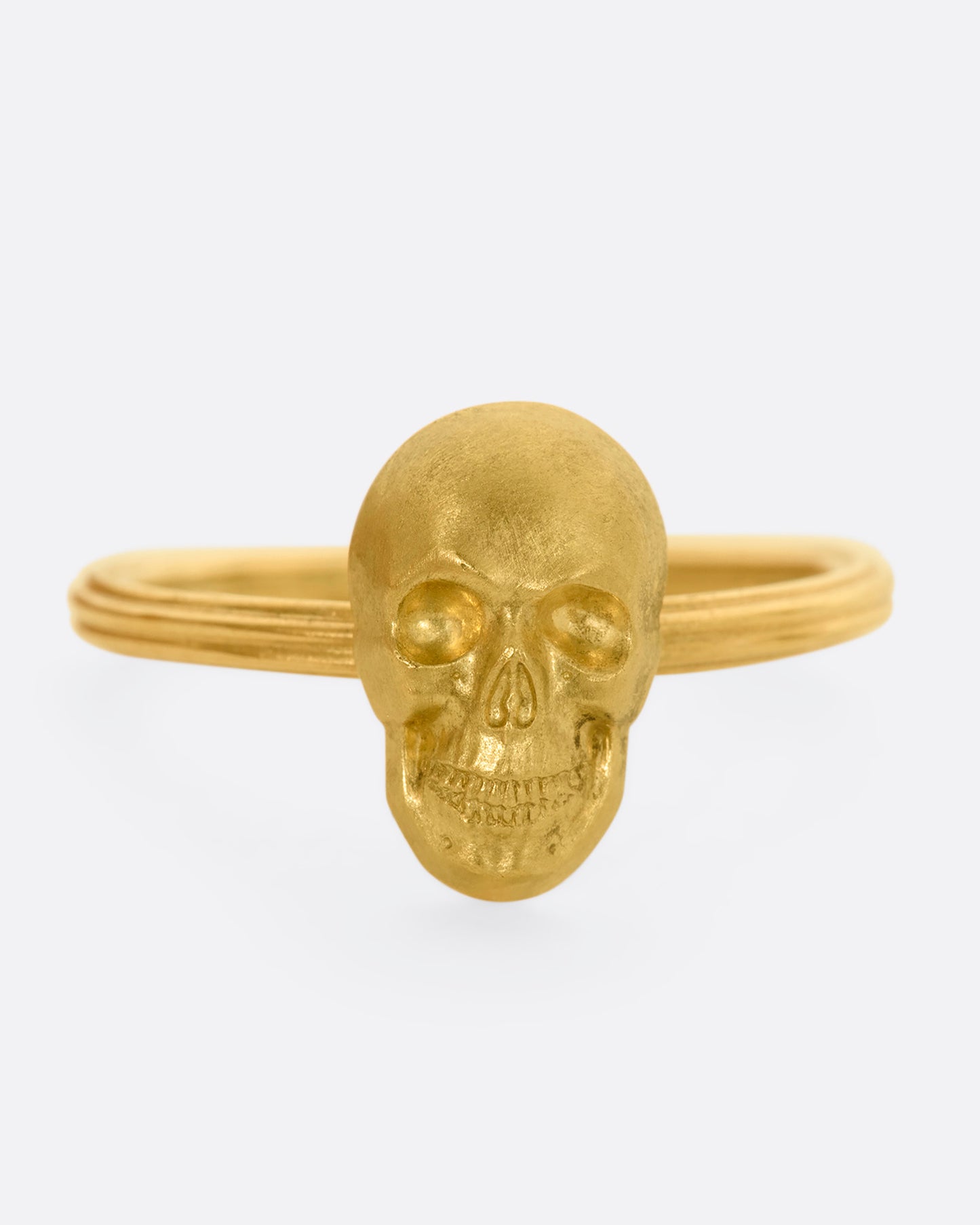 Front view of yellow gold ring with a sculpted skull charm on a round fluted band.