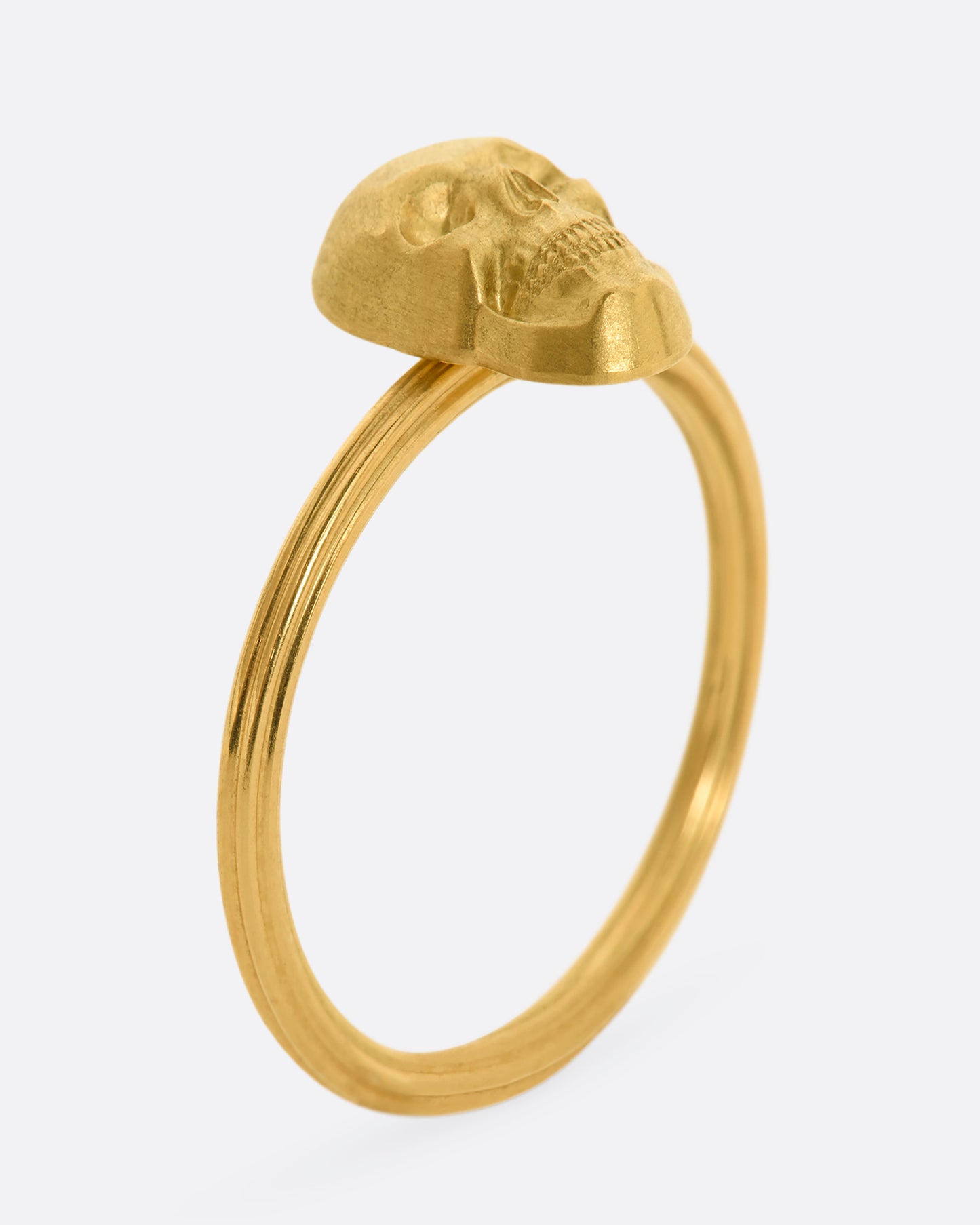 Standing side view of yellow gold ring with a sculpted skull charm on a round fluted band.