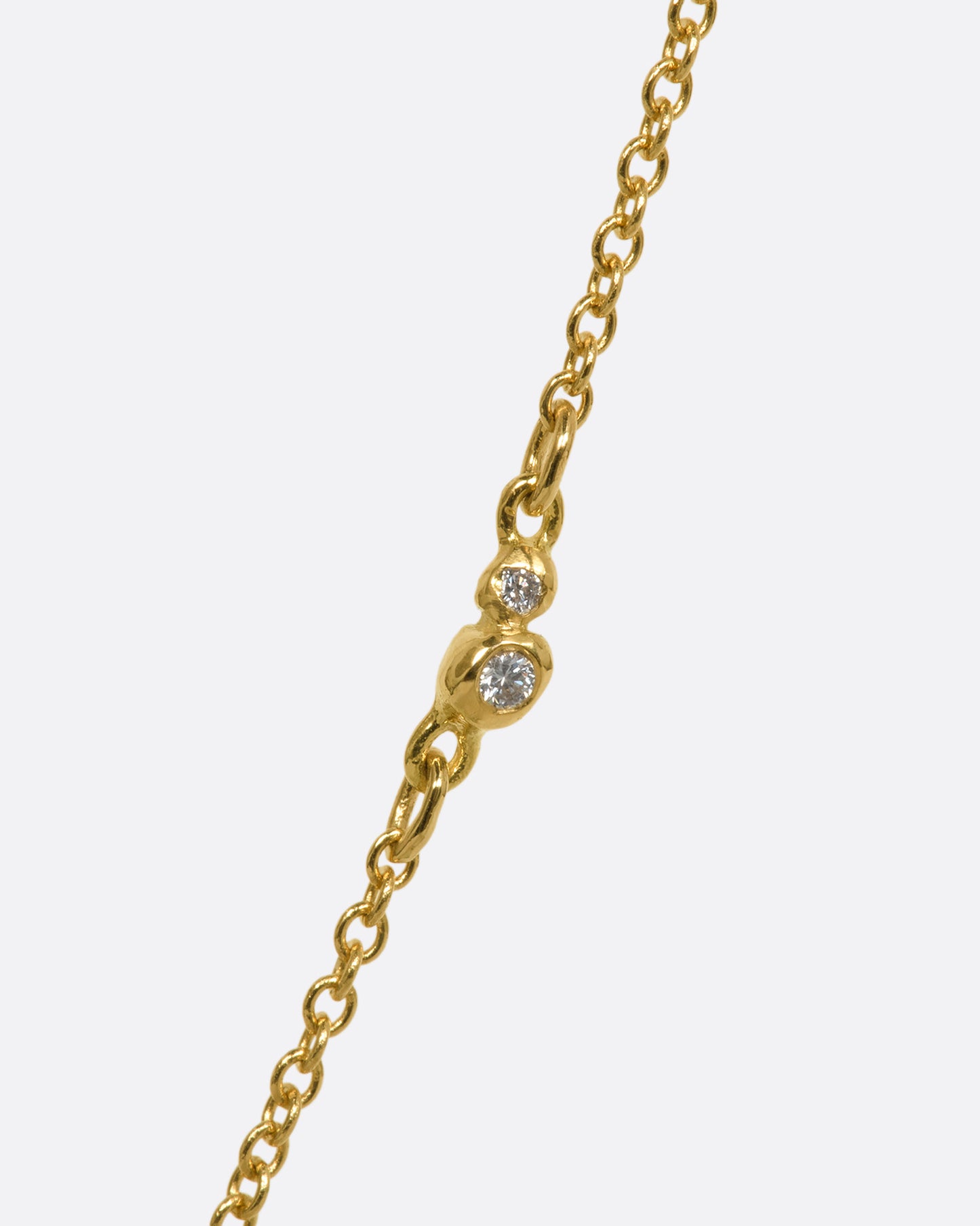 A yellow gold necklace with a rose cut solitaire diamond pendant and a cluster of diamonds on the chain. View of the two diamond cluster.