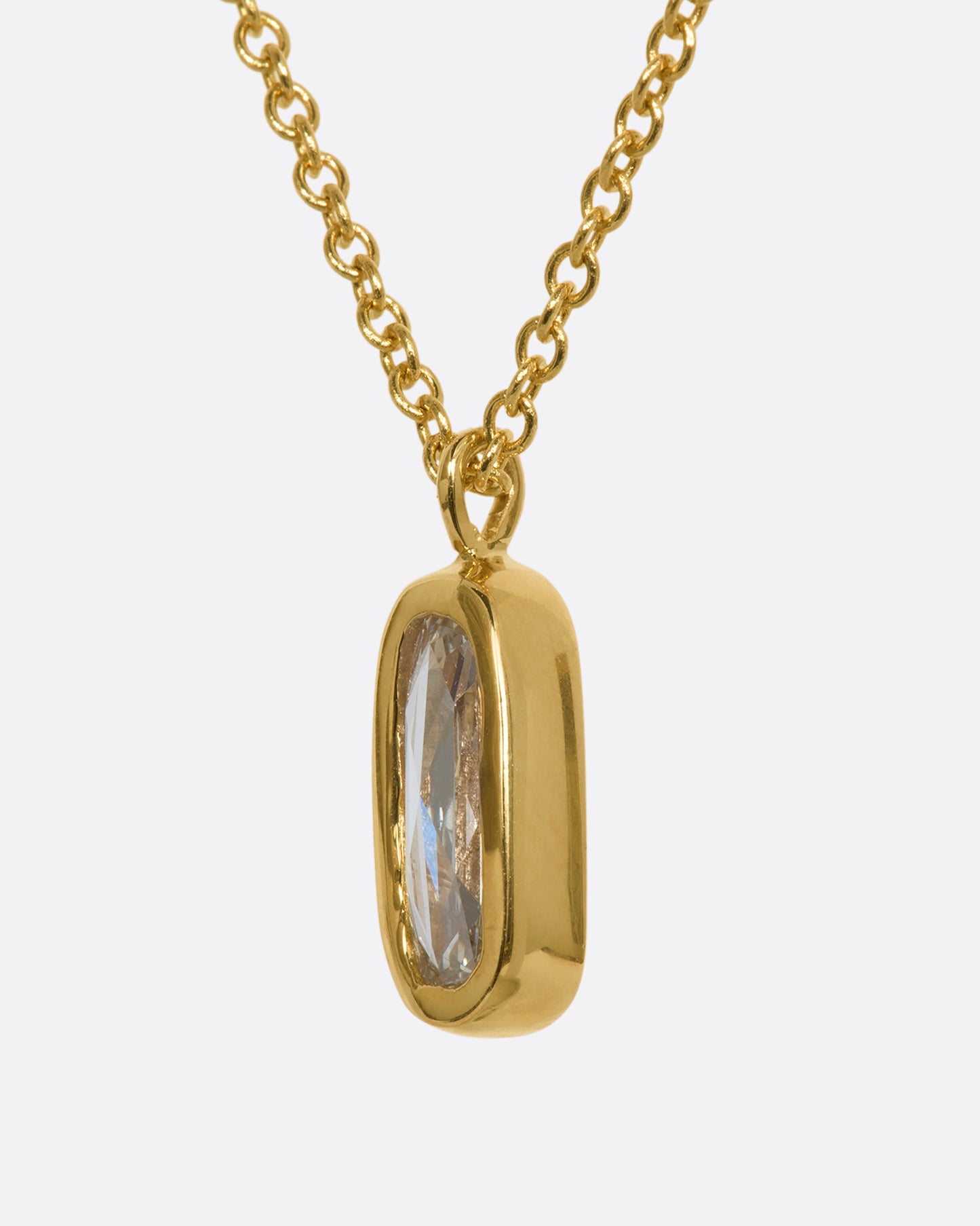A yellow gold necklace with a rose cut solitaire diamond pendant and a cluster of diamonds on the chain. View from the side.