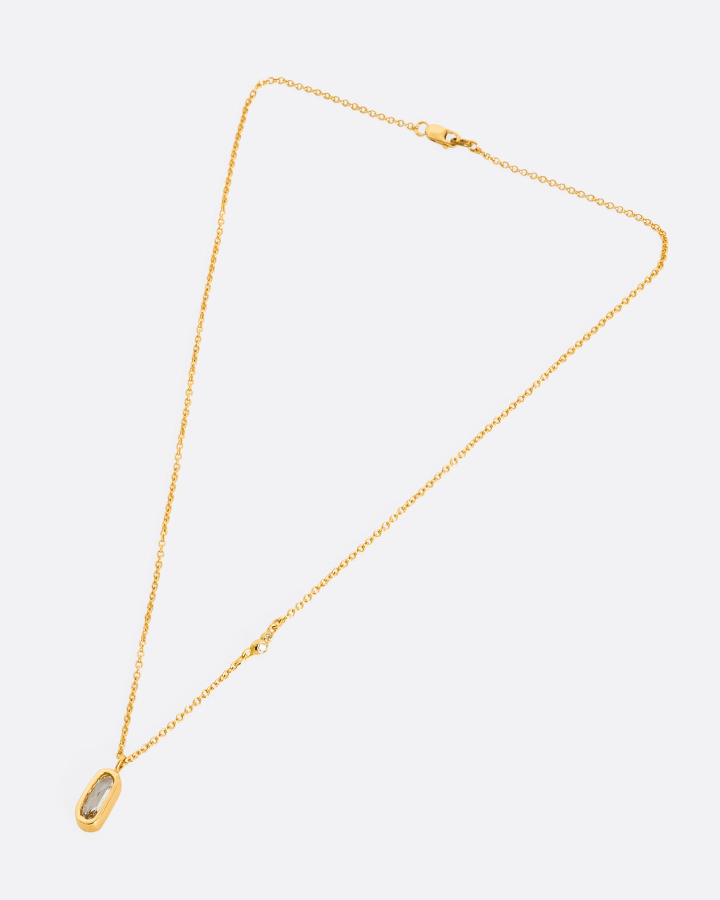 A yellow gold necklace with a rose cut solitaire diamond pendant and a cluster of diamonds on the chain. View of the entire necklace, laying flat from above.