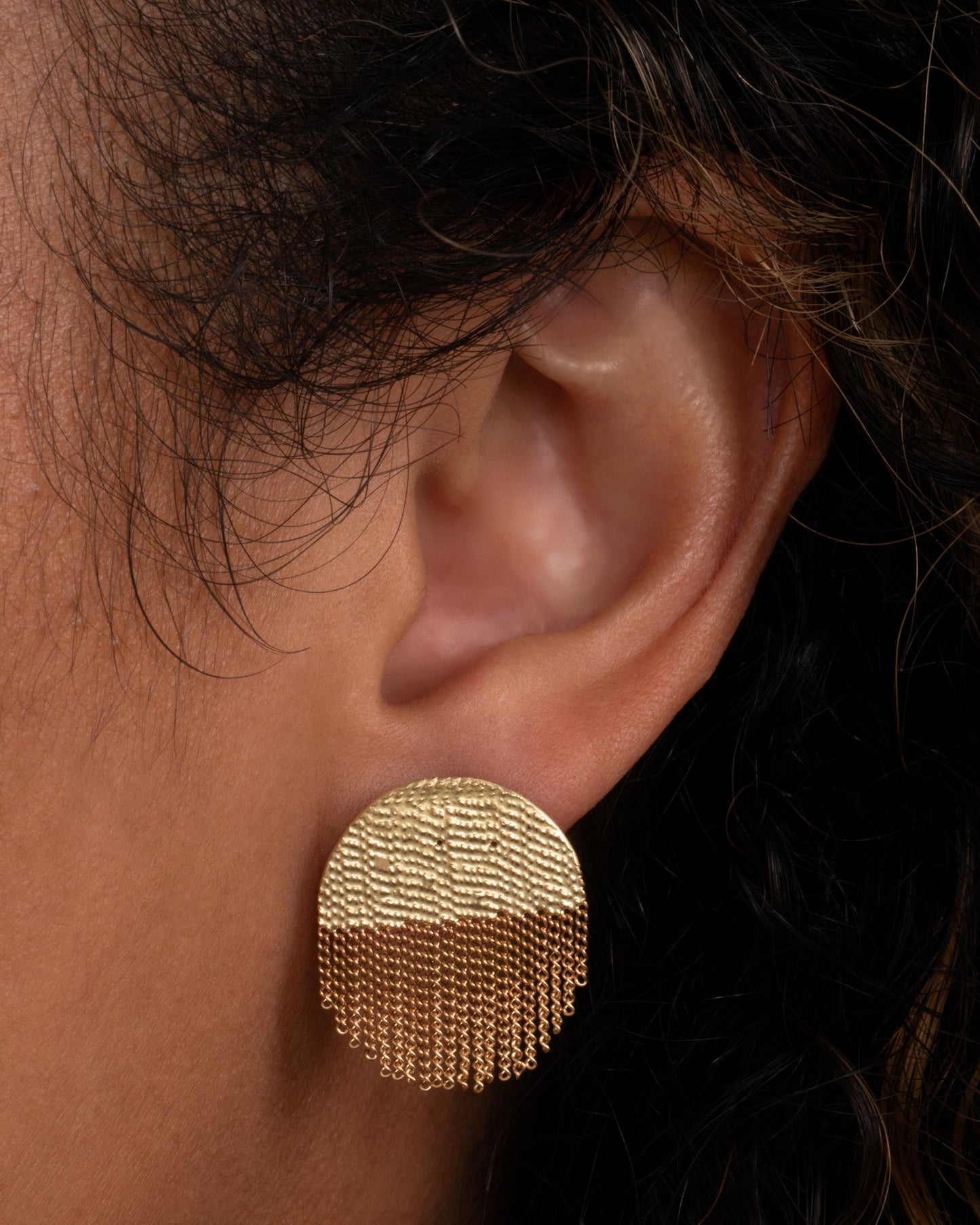 A yellow gold circular stud back earring that's half solid and half fringe chain. Shown in an ear.