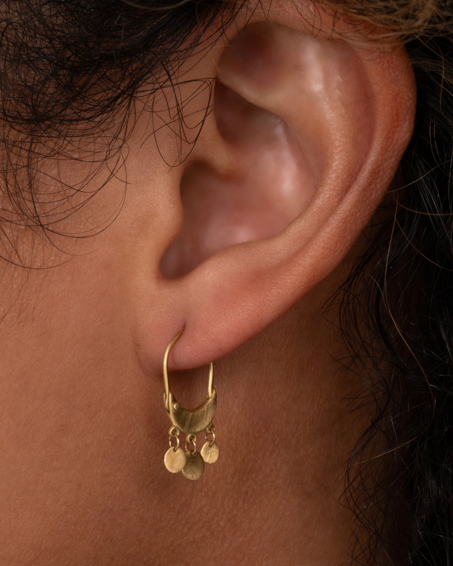 A pair of yellow gold chandelier hoop earrings shown on an ear.