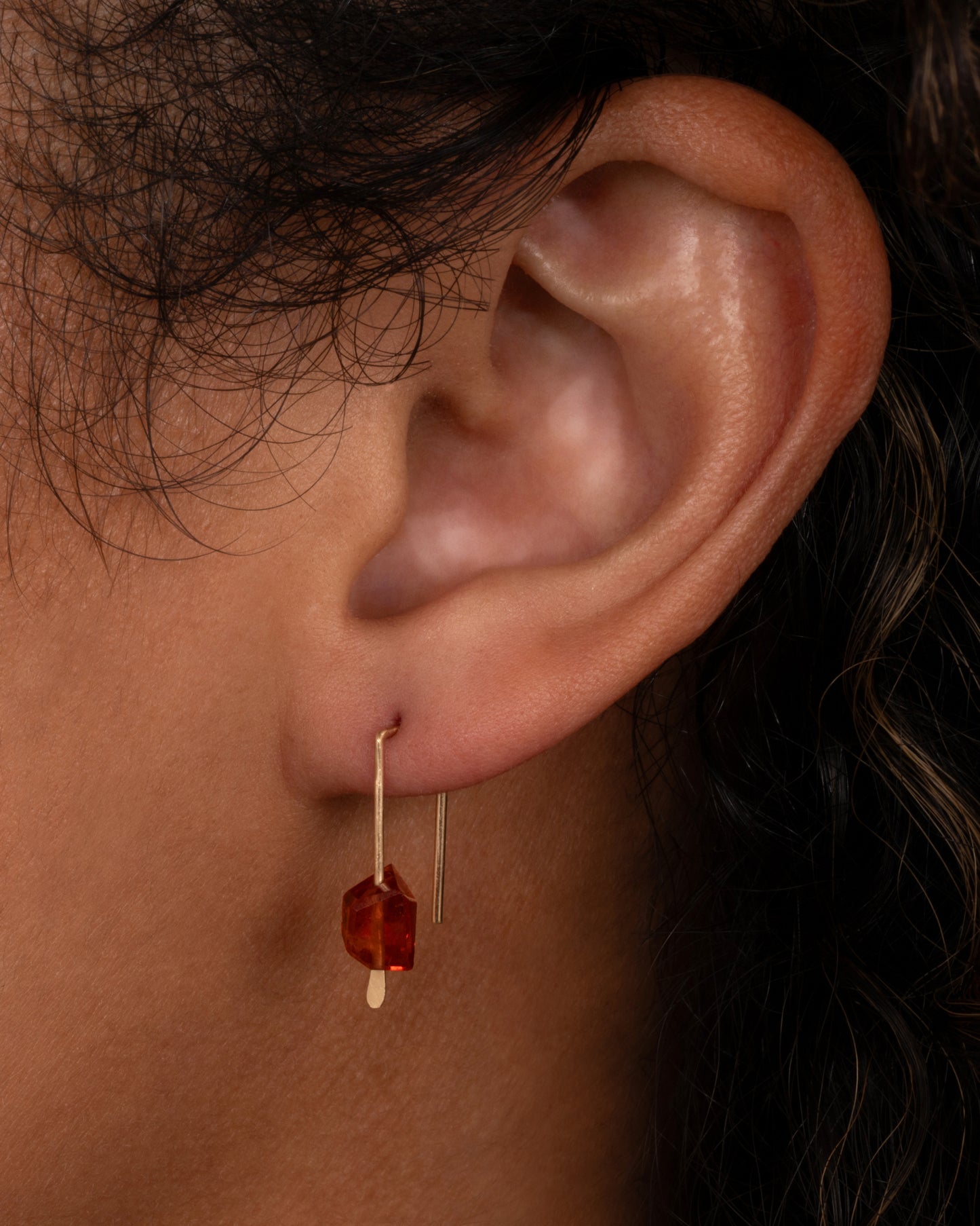A yellow gold hook earring with an angular hessonite garnet, shown on an ear.