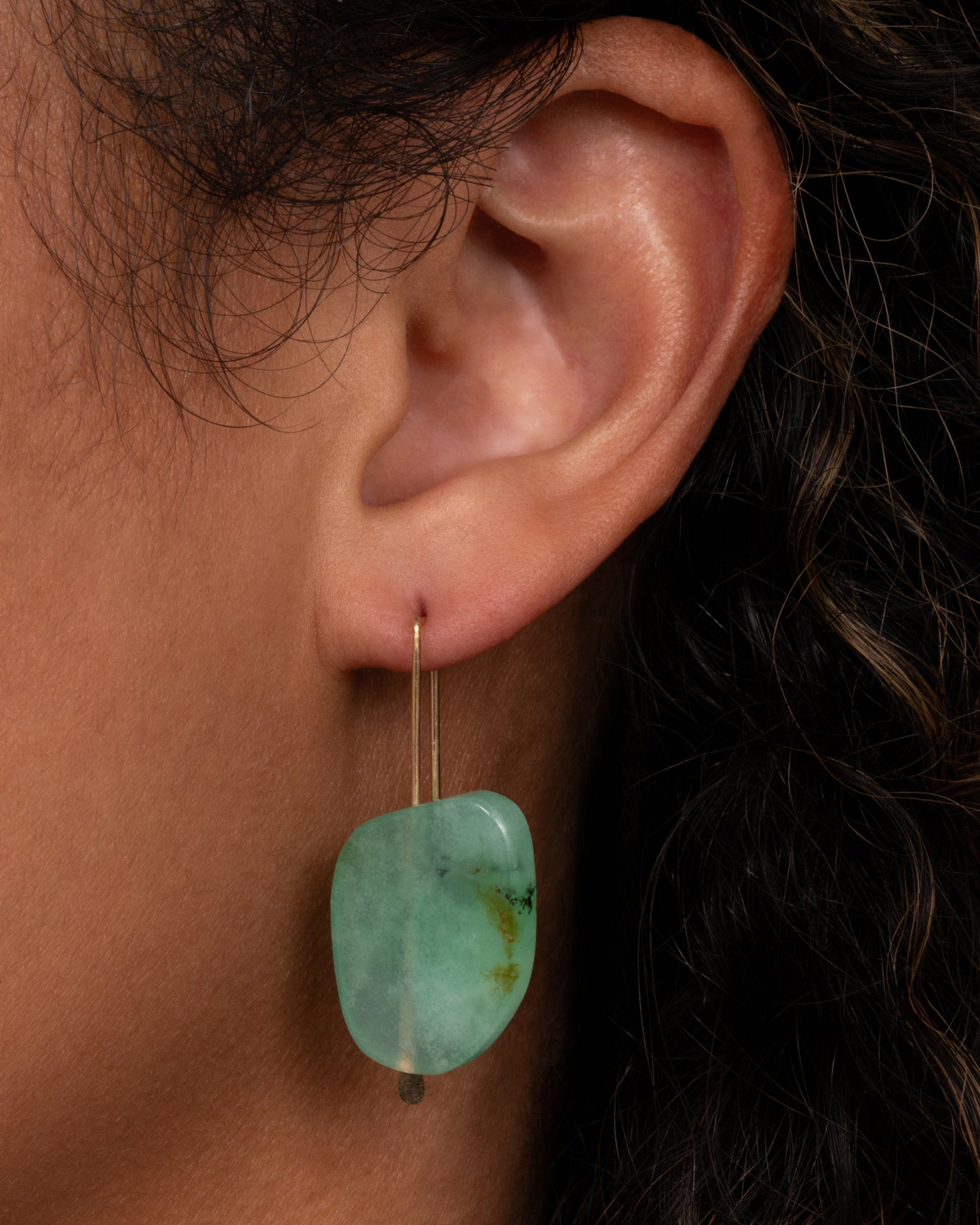 A yellow gold hook earring with a single freeform chrysoprase.
Shown on an ear.