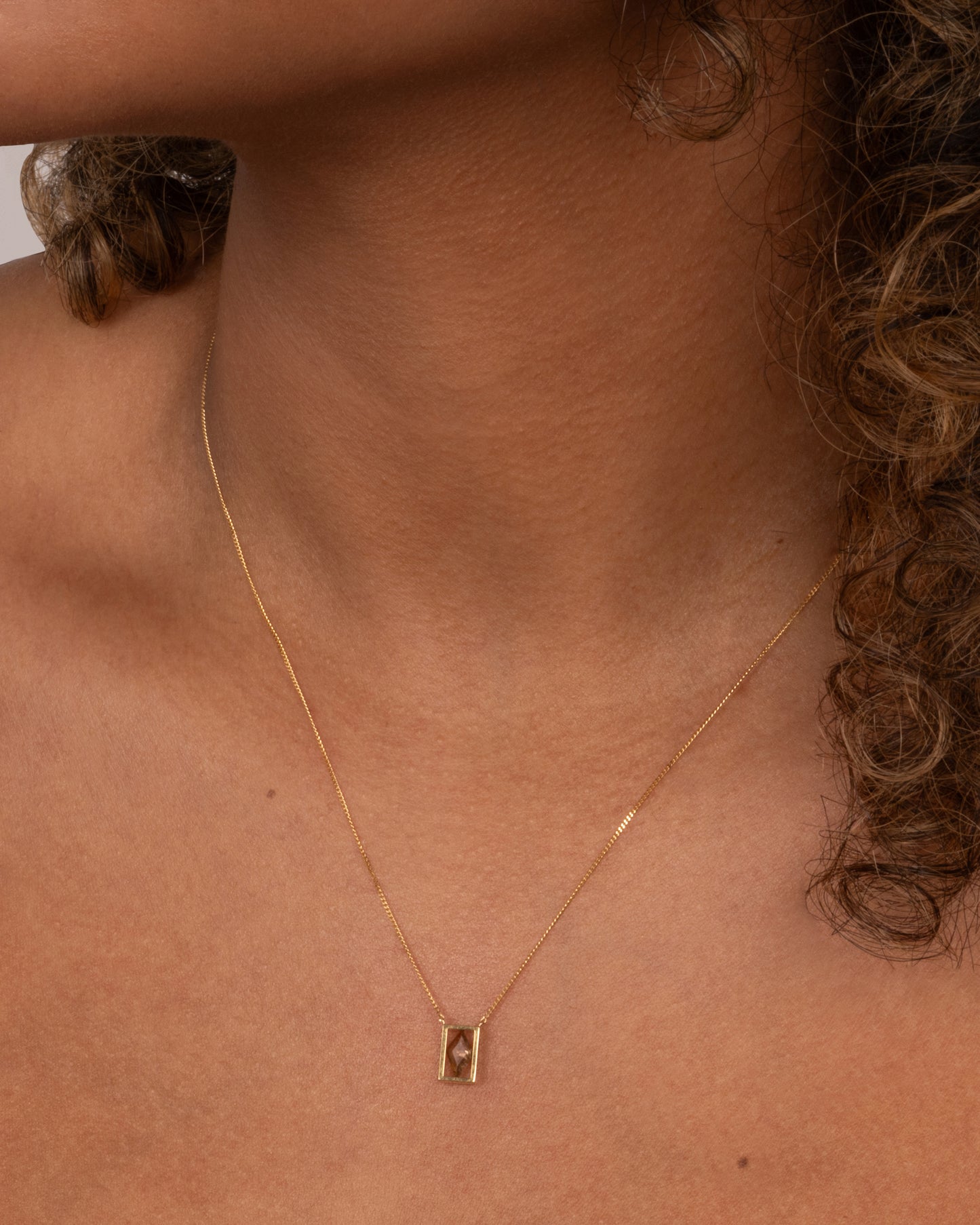 A yellow gold cable chain necklace with a rhombus shaped diamond in an open rectangular setting, shown on an person.