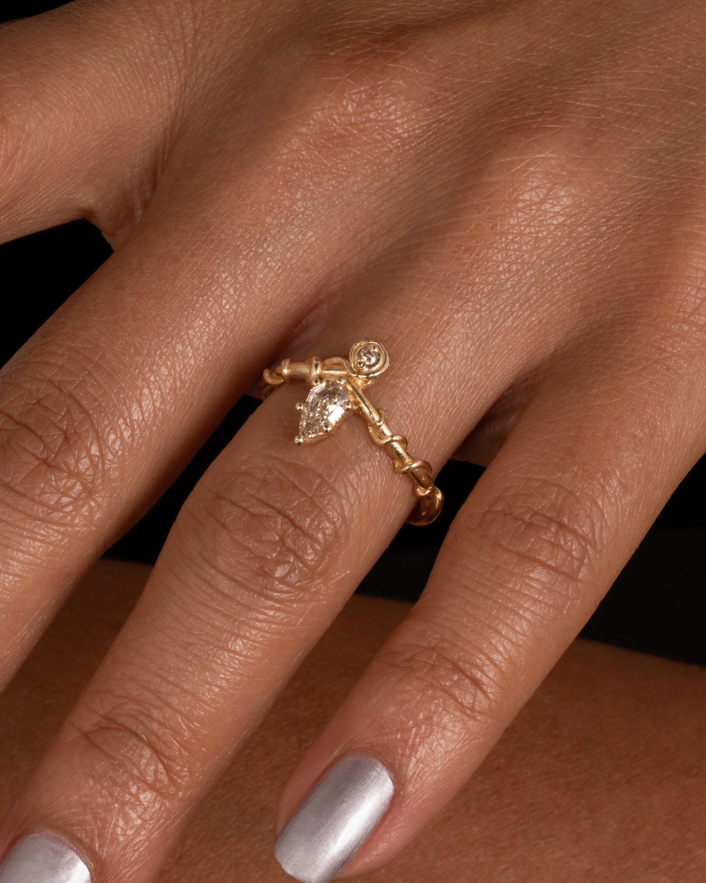 A yellow gold ring with a vine wrapped band and two stacked diamonds, one pear one round. Shown on a finger.