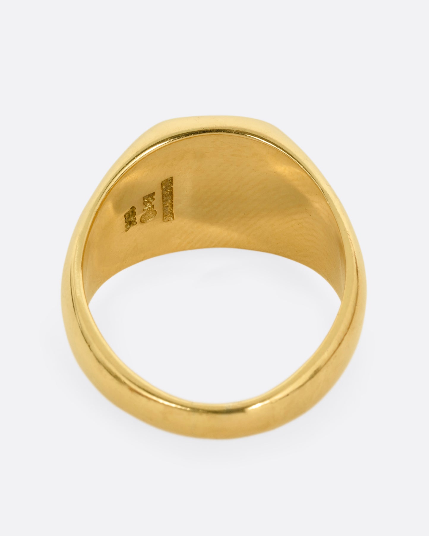 A yellow gold signet ring with a square onyx inlaid face and a diagonal split through its center. Shown from the back.