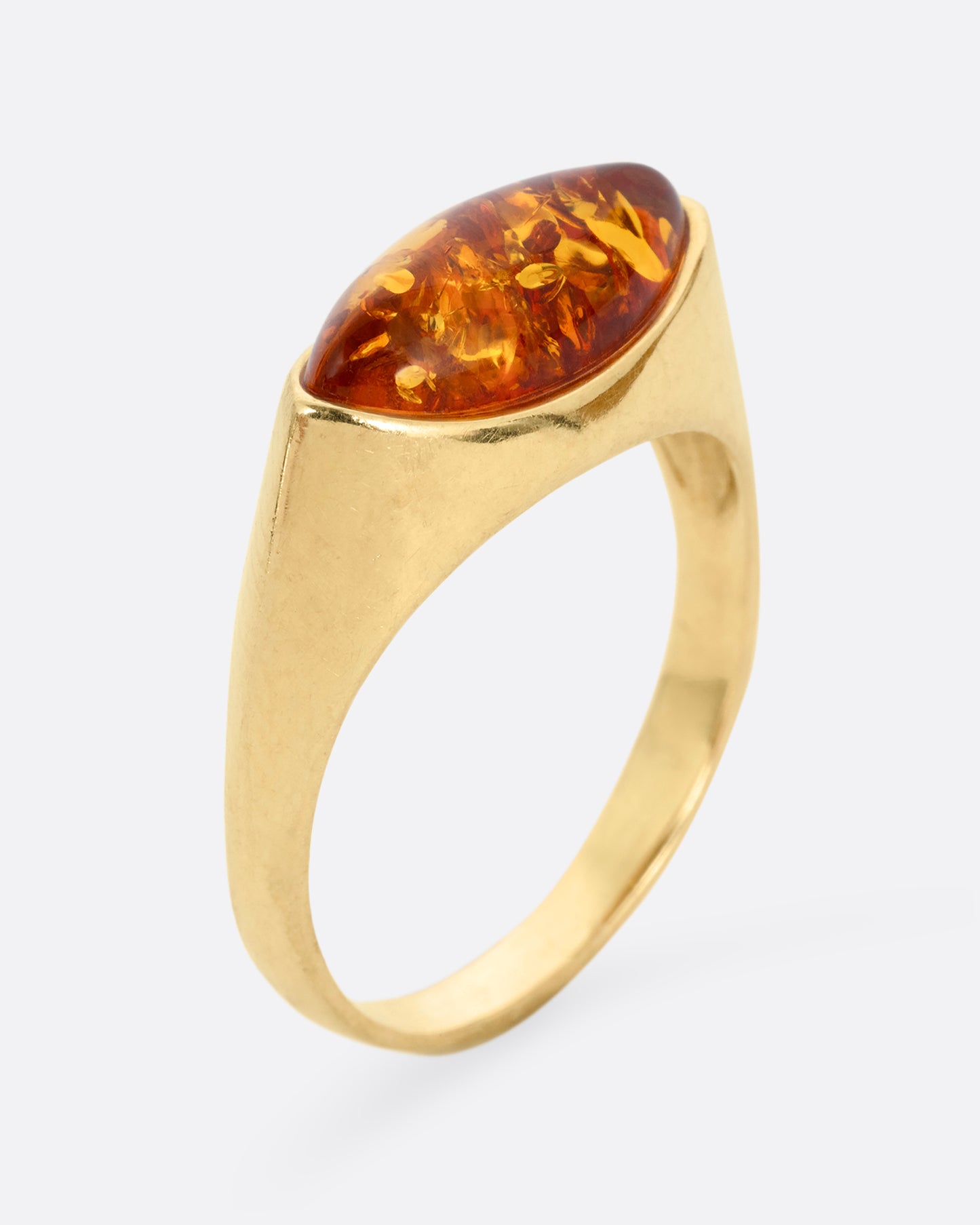 A yellow gold ring with an oval amber, shown standing up from the side.