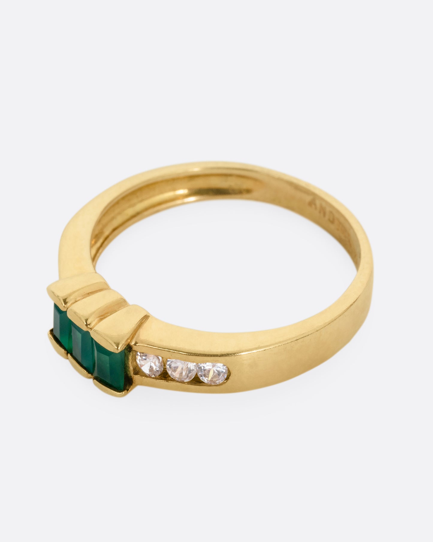 A yellow gold ring with six white diamonds and three emerald baguettes, shown from the side.