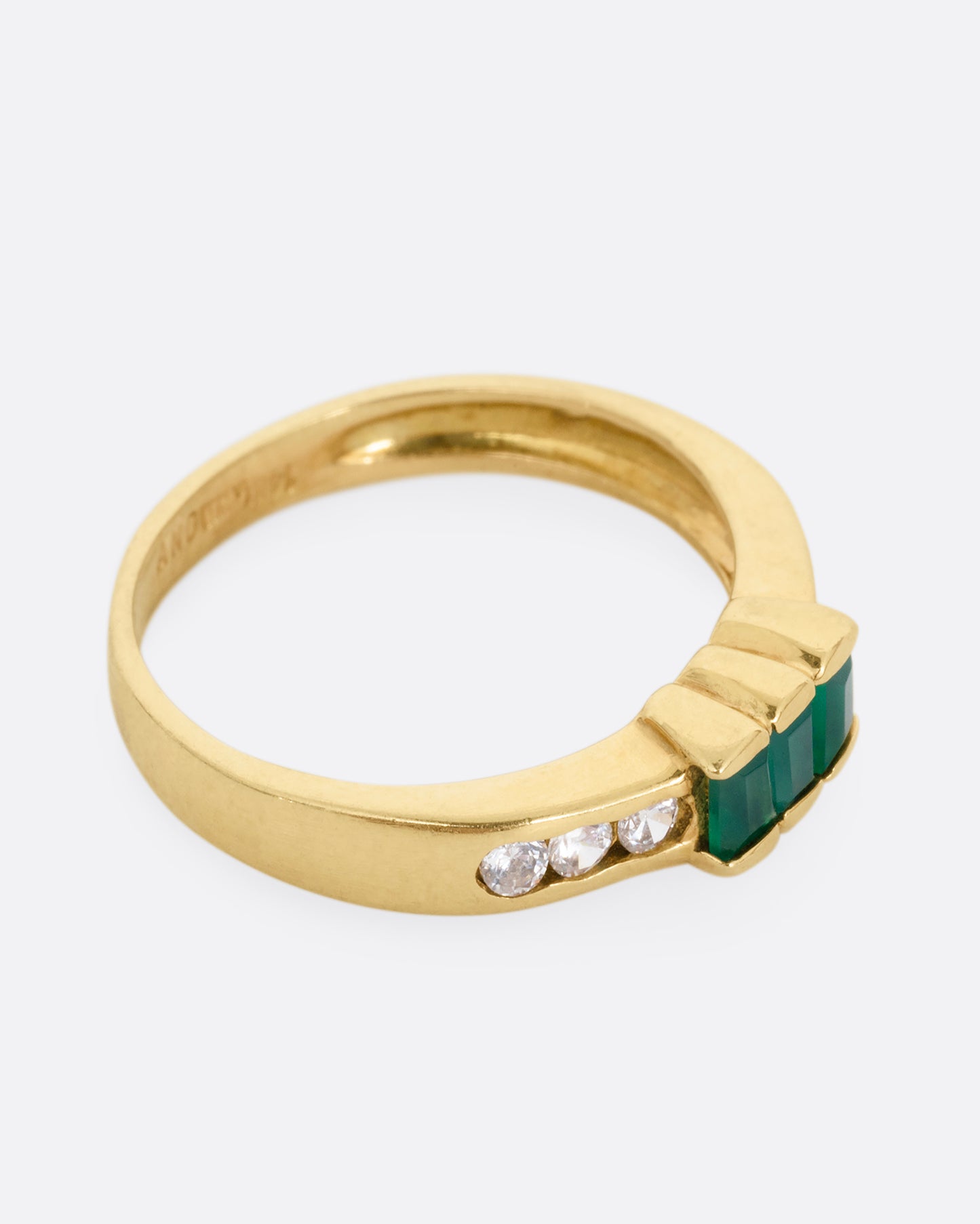 A yellow gold ring with six white diamonds and three emerald baguettes, shown from the side.