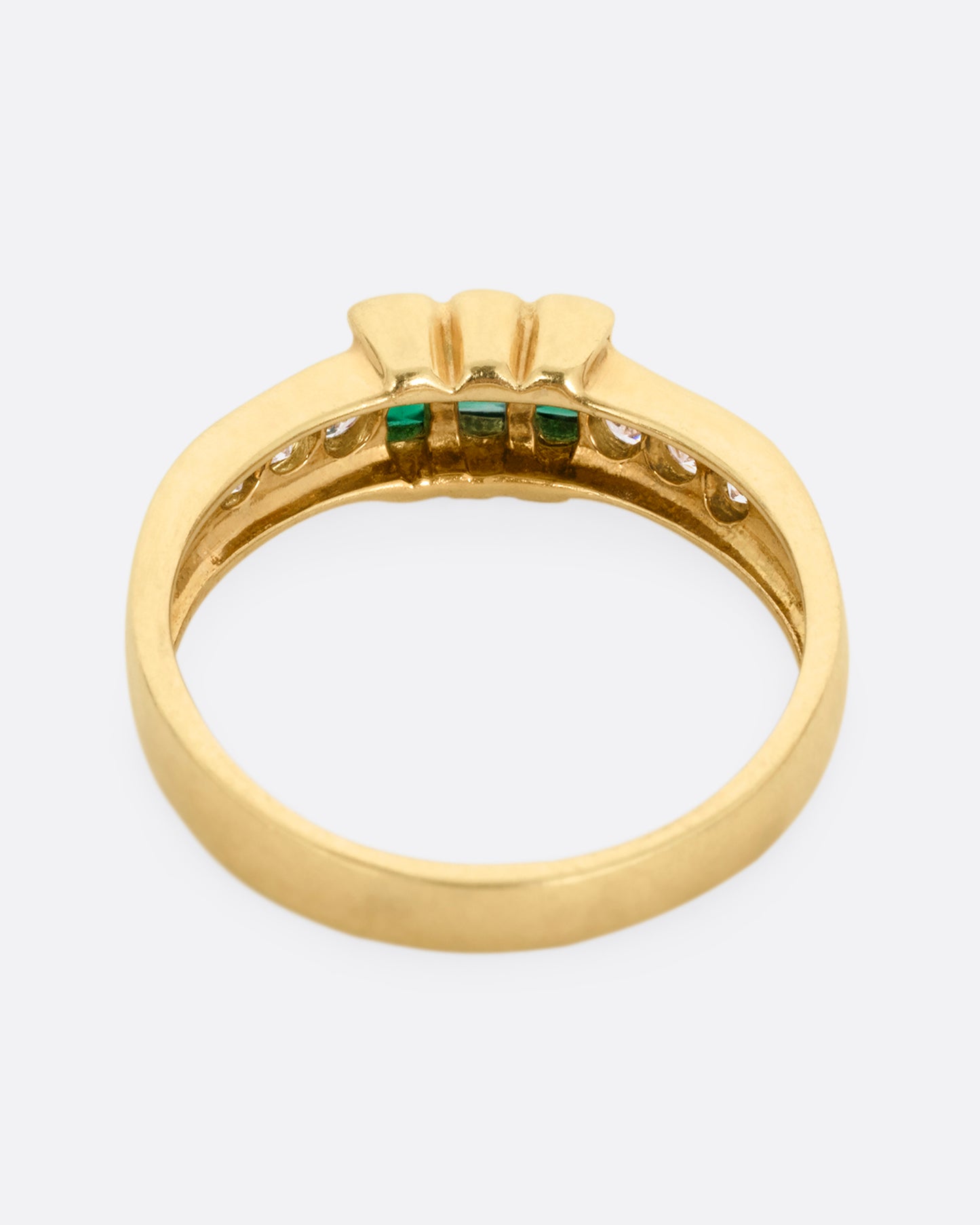 A yellow gold ring with six white diamonds and three emerald baguettes, shown from the back.