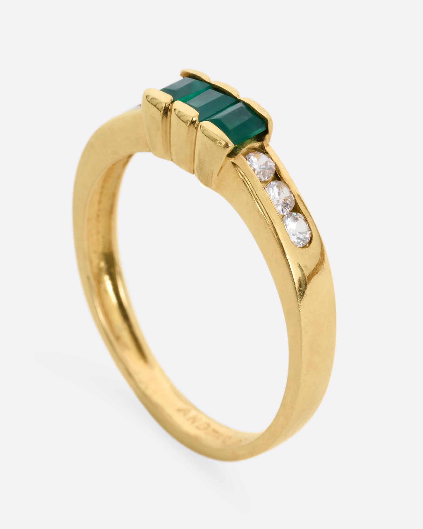 A yellow gold ring with six white diamonds and three emerald baguettes, shown standing up from the side.