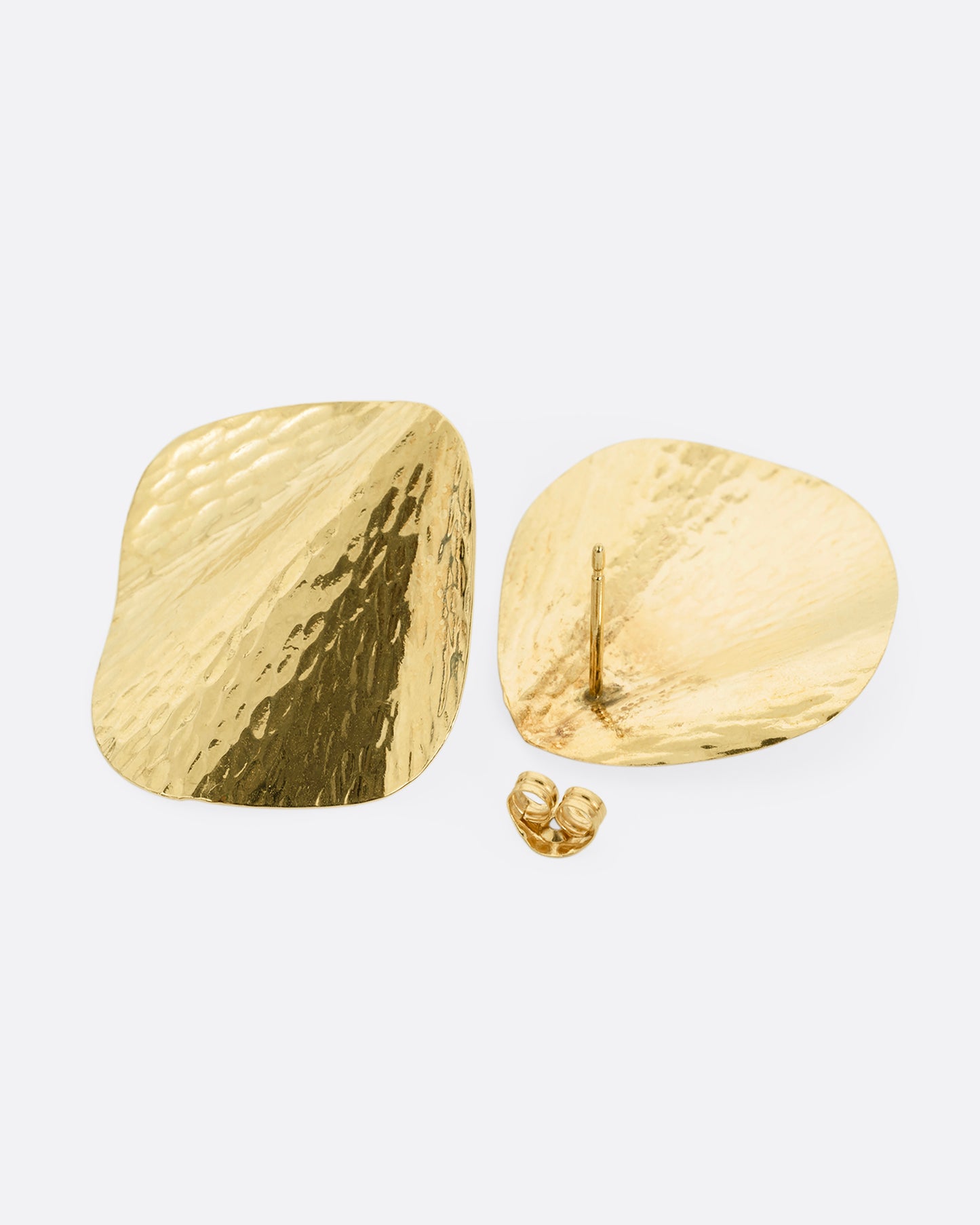 A pair of yellow gold stud earrings with a textural finish and wavy silhouette, shown lying flat- one earring from the front, the other open from the back.