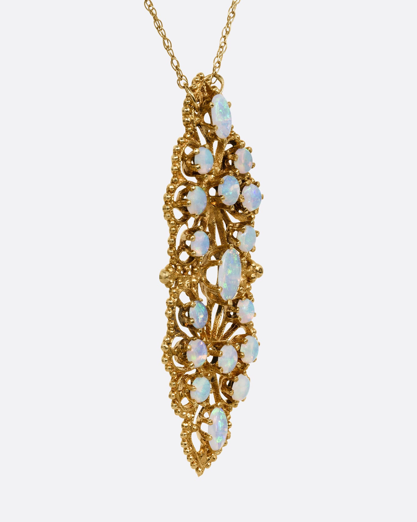 A yellow gold opal studded floral pendant, shown from the side on a cable chain.