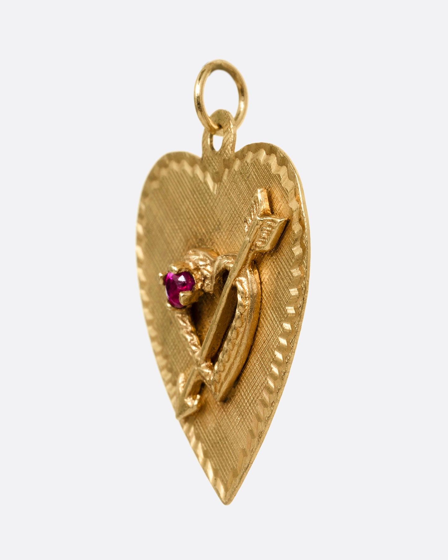 A yellow gold heart shaped pendant with a ruby and small arrow- stricken heart at the center. Shown from the side.
