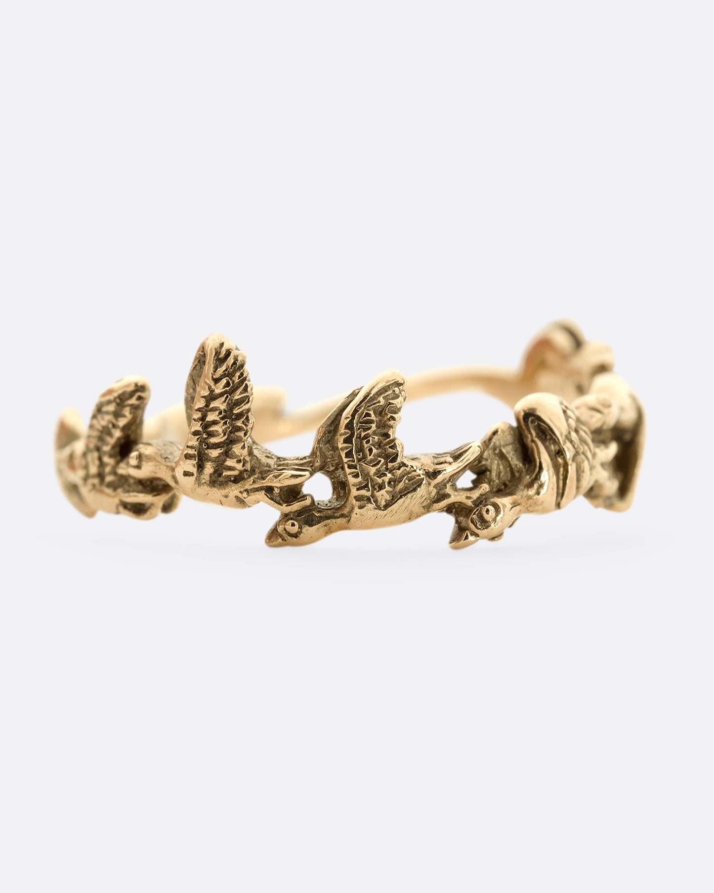 A yellow gold ring with birds flying around the majority of the band. Shown from the front.